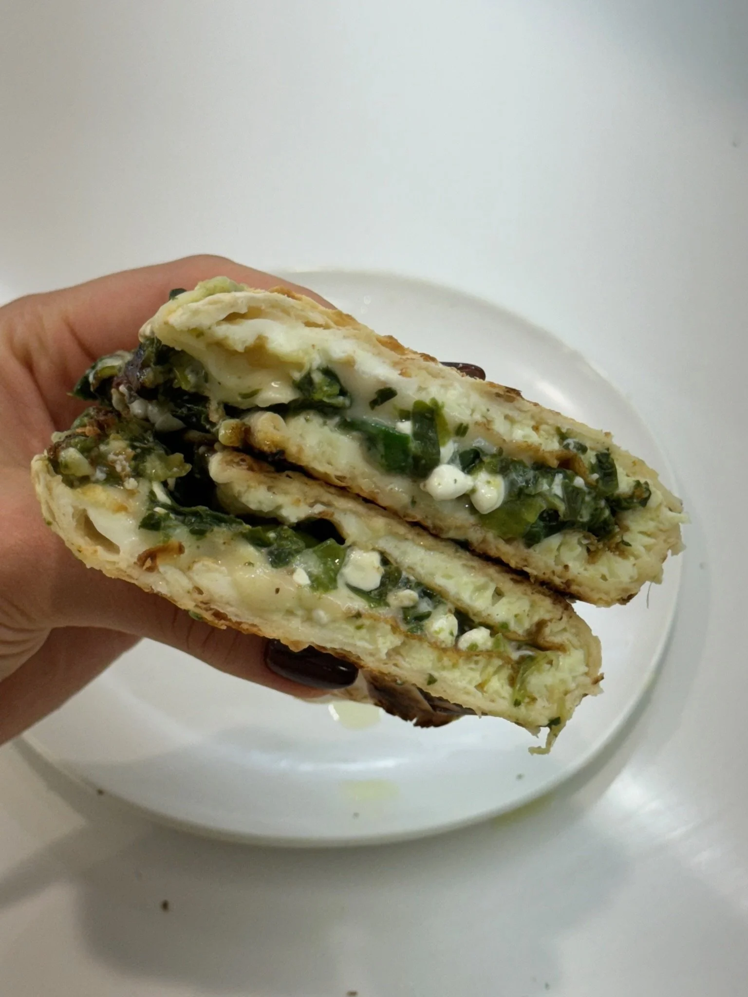 Close-up of a spinach and cheese stuffed flatbread sandwich cut in half, held over a white plate.