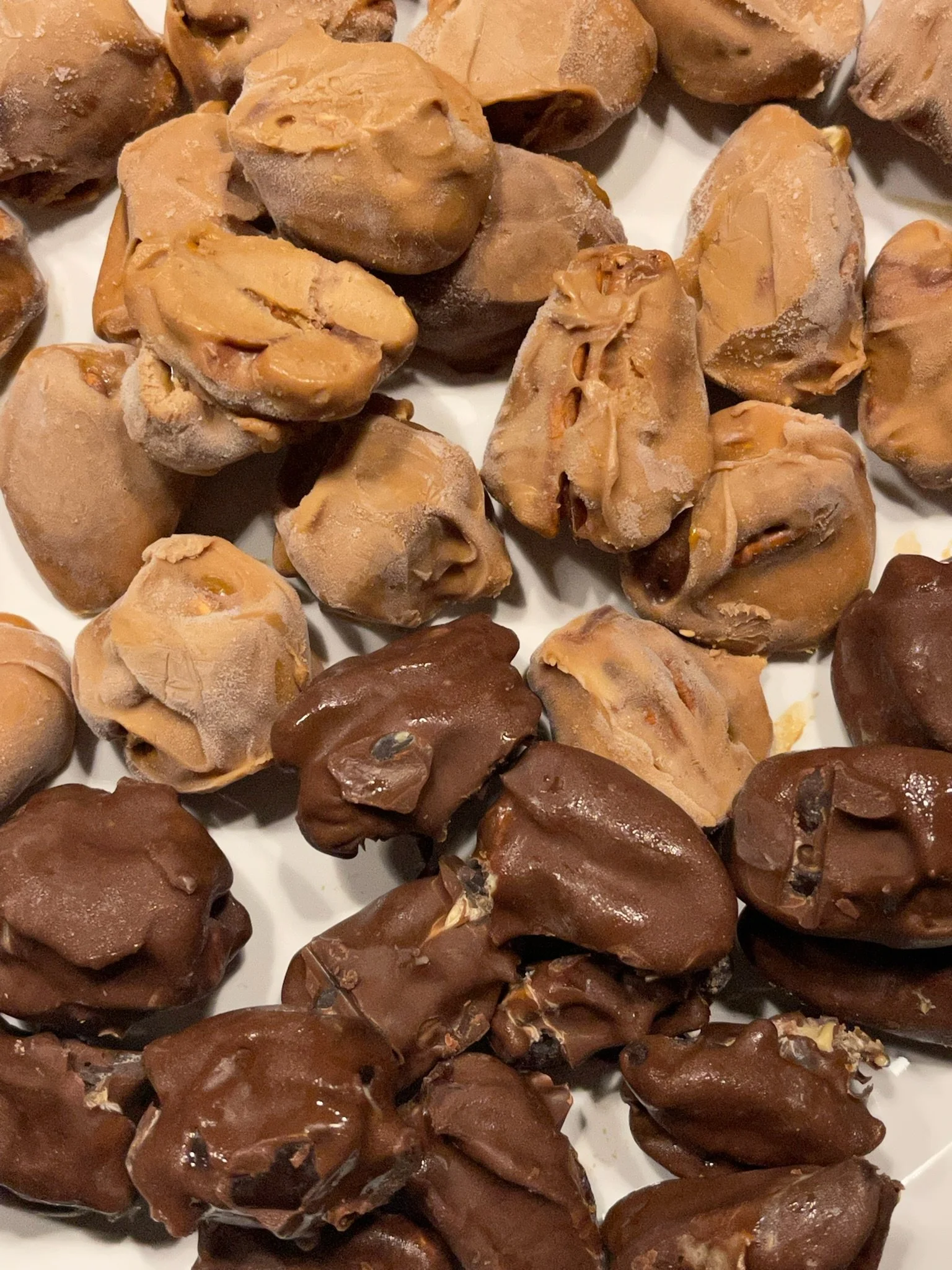 Close-up of assorted chocolate candies, including peanut butter and chocolate-coated varieties on a white plate.