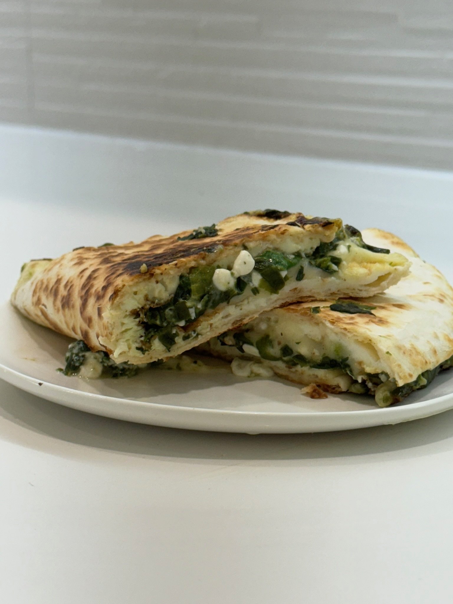A plate with two pieces of quesadilla filled with cheese and green vegetables, with a toasted and slightly charred tortilla exterior.