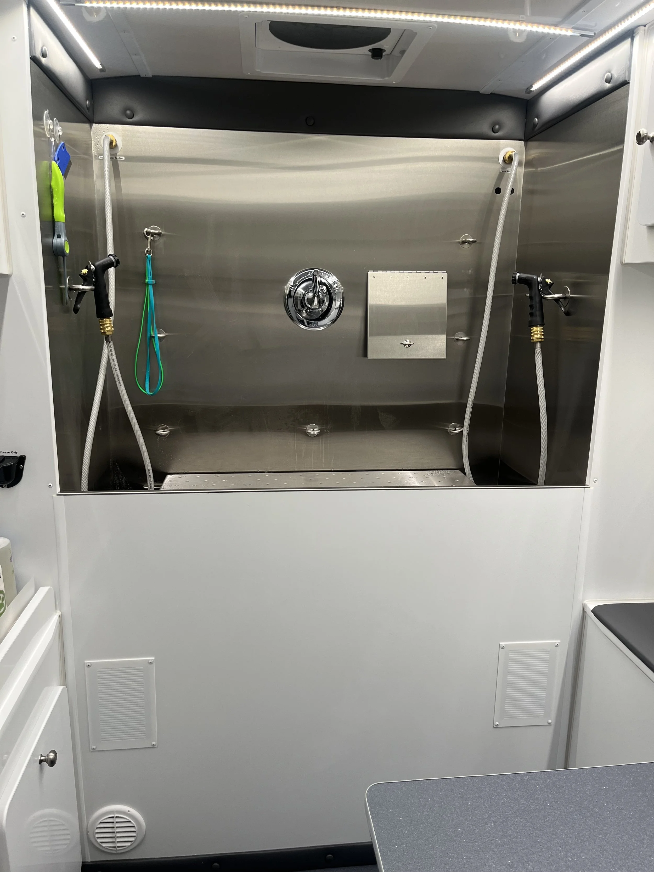 Interior of a portable spray wash station or decontamination shower with hoses, nozzles, and control panel.