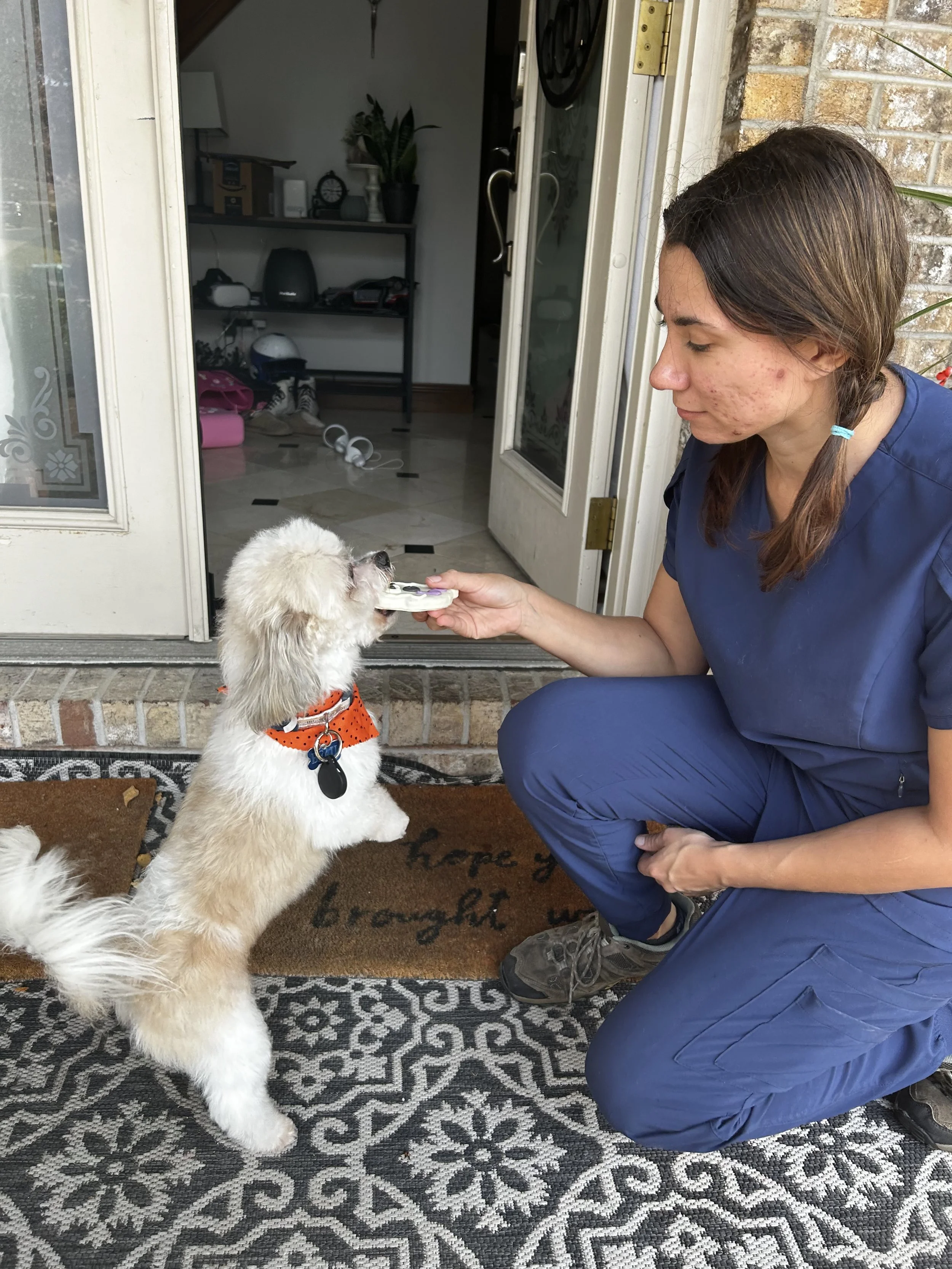 A woman with gray hair wearing a blue short-sleeve sweater and beige pants, sitting on a bench against a plain beige wall, looking to the side with shadows cast behind him.