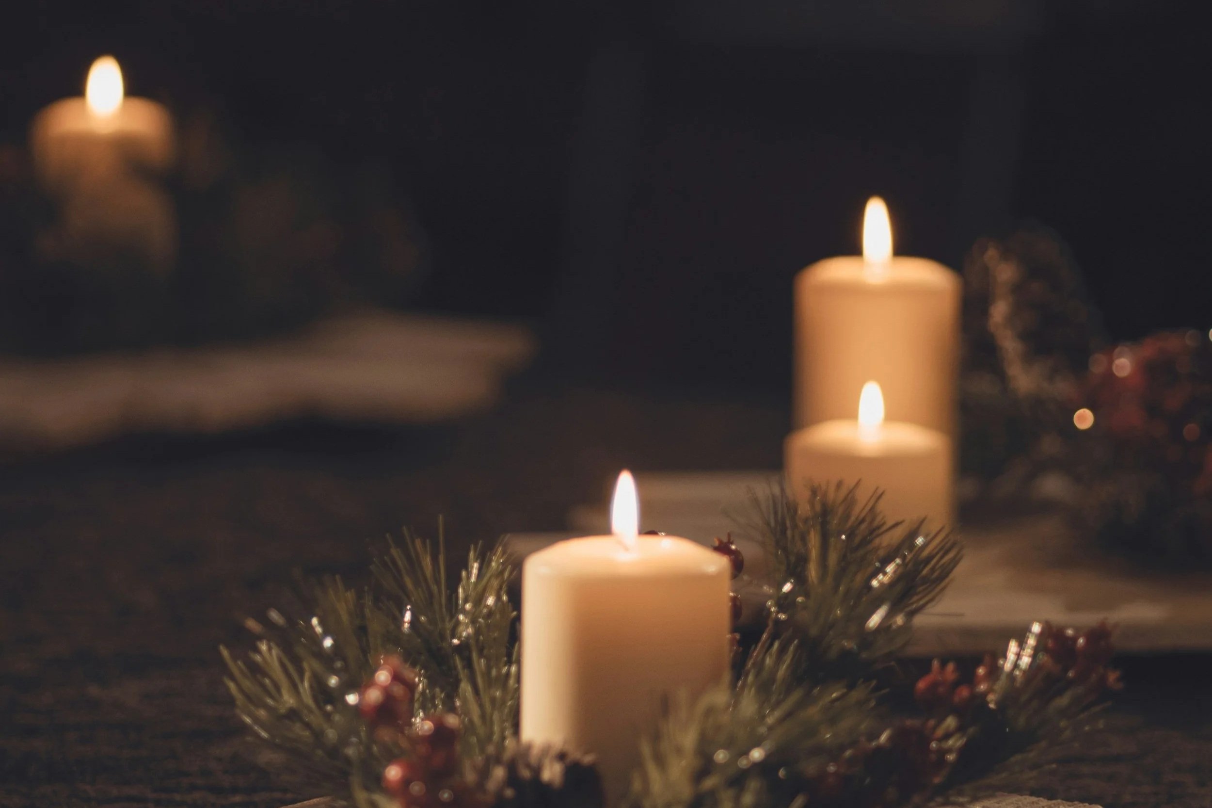 Tres velas encendidas rodeadas de ramas de pino y decoraciones navideñas en un ambiente oscuro.