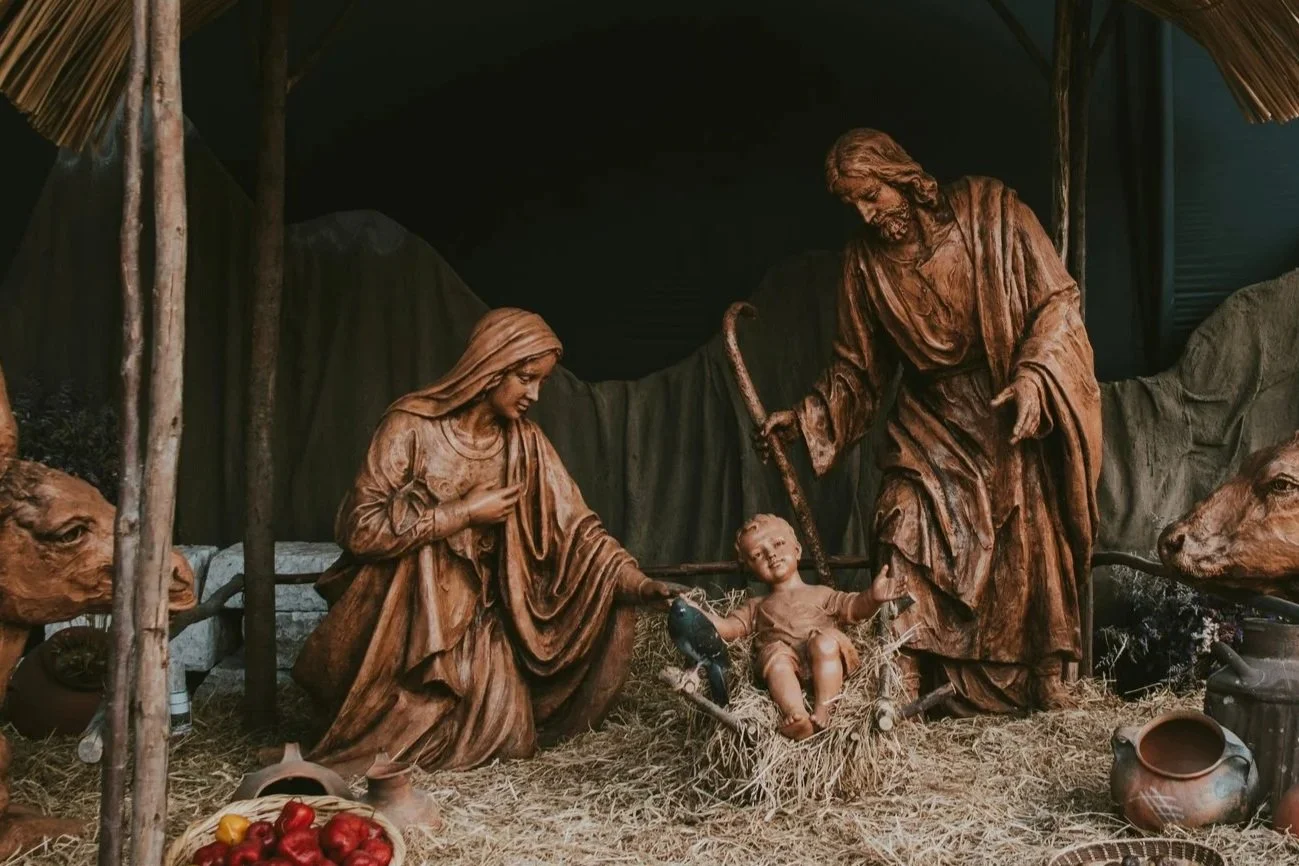 Escultura de la Sagrada Familia con Jesús niño en un pesebre, rodeada de animales y decoraciones rurales.