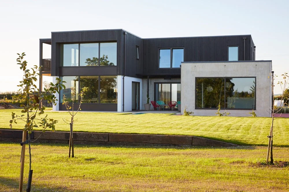 Modern two-story house with large glass windows and a front lawn with small trees