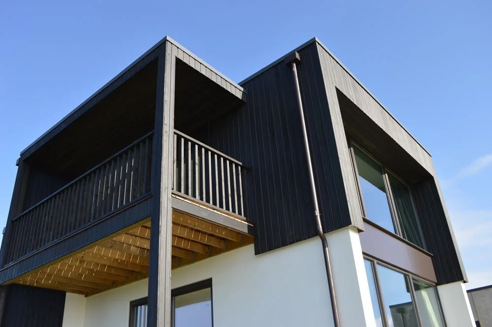 Modern two-story building with black wooden exterior and large windows, featuring a balcony on the upper level.