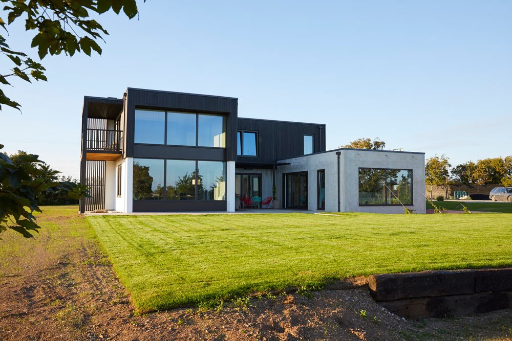 Modern two-story house with large glass windows and a well-maintained green lawn in the front yard.