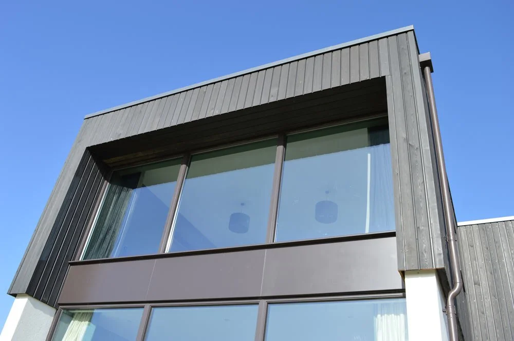 Modern building with large glass windows and black exterior siding under a clear blue sky.