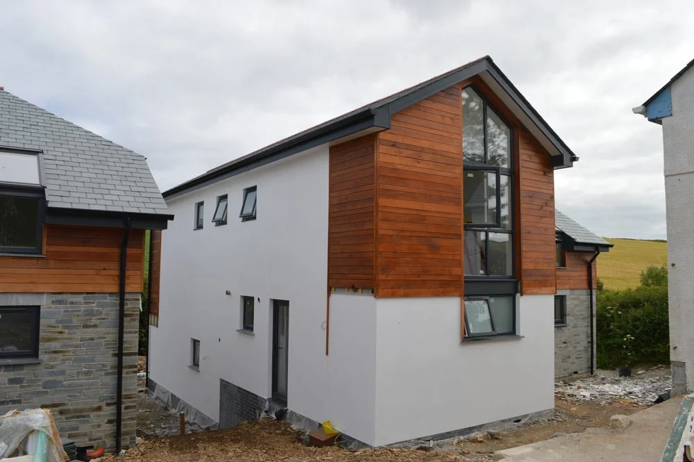 Modern house with white and wooden exterior, multiple windows, on a cloudy day, neighboring buildings nearby.