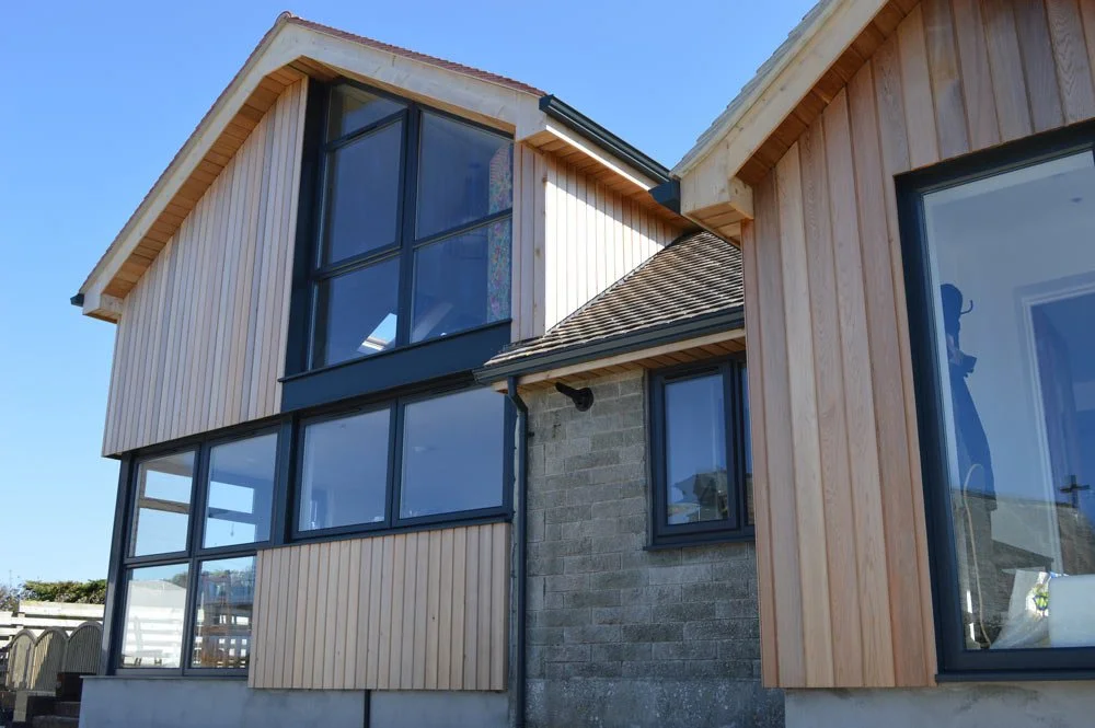 Modern residential house with wooden and brick exterior, large windows, and a sloped roof.