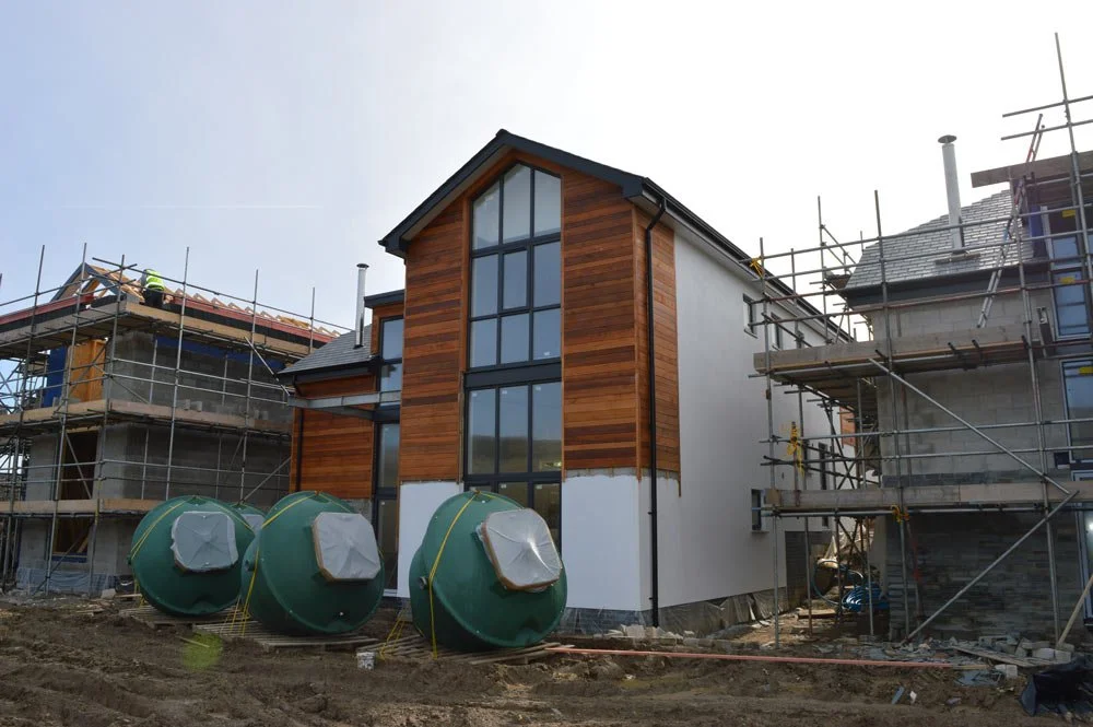Newly constructed house with wood paneling and large windows, surrounded by scaffolding and construction materials.