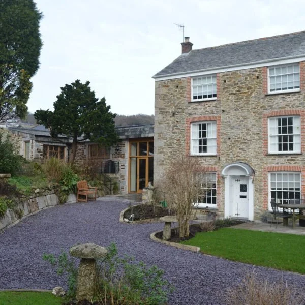 A stone house with a front door, multiple windows, and a sloped roof, surrounded by a landscaped yard with a gravel pathway, trees, and outdoor furniture.