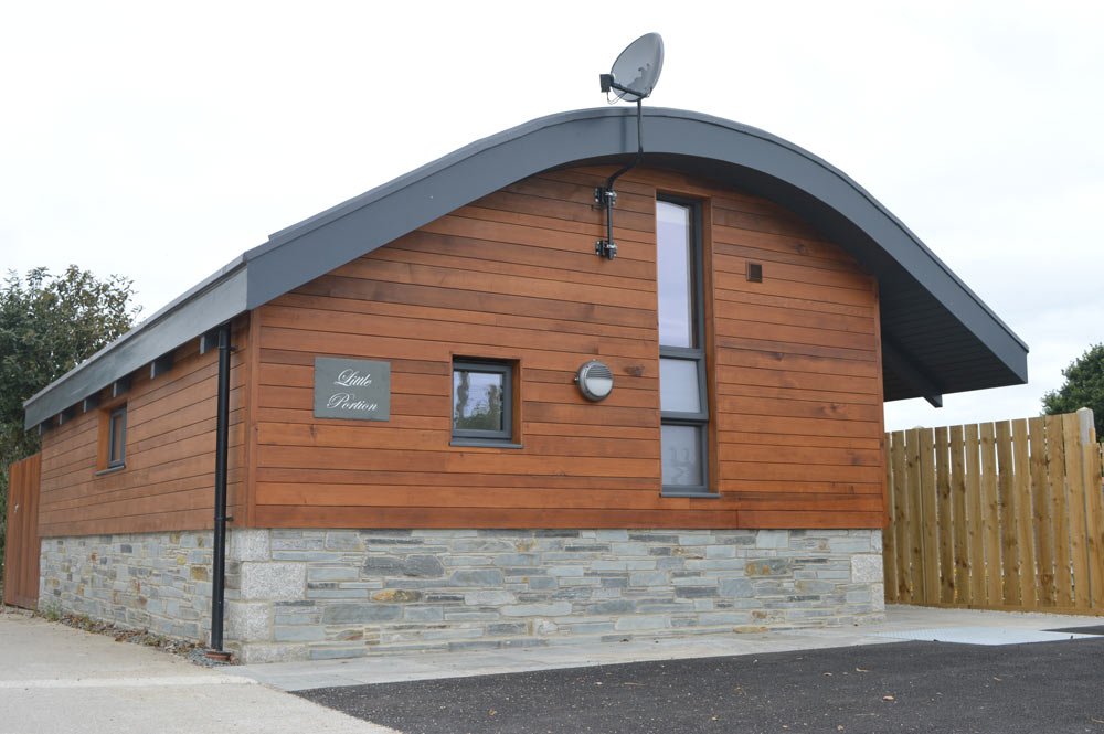 A small house with a curved gray roof, wooden siding, stone foundation, and a satellite dish on top.
