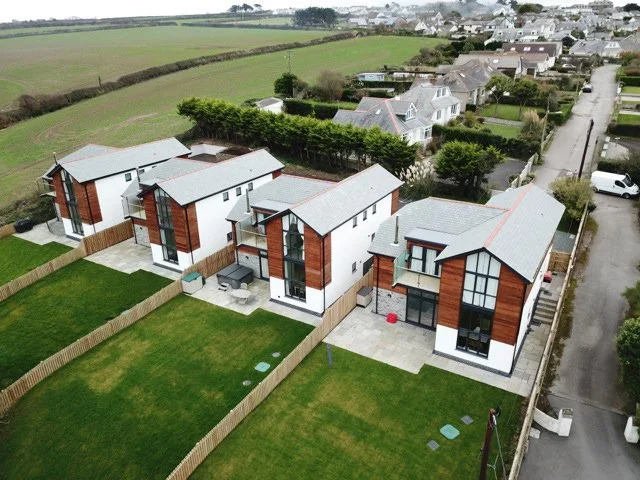 Aerial view of four modern houses with large windows, fenced yards, and well-maintained lawns in a suburban neighborhood.