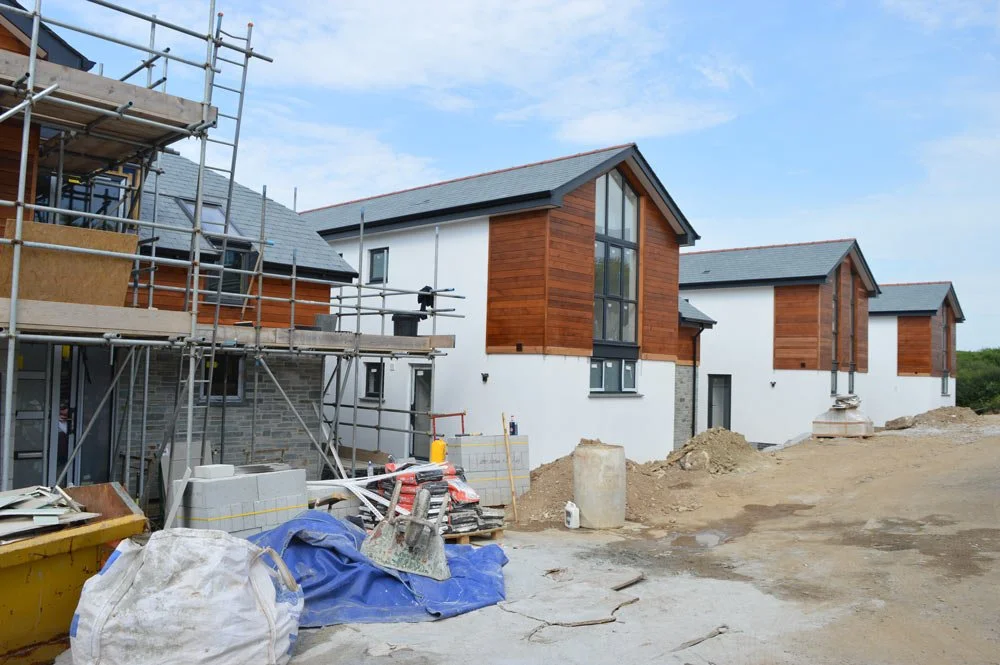 Construction site of modern houses with scaffolding, wood paneling, and construction materials on the ground.