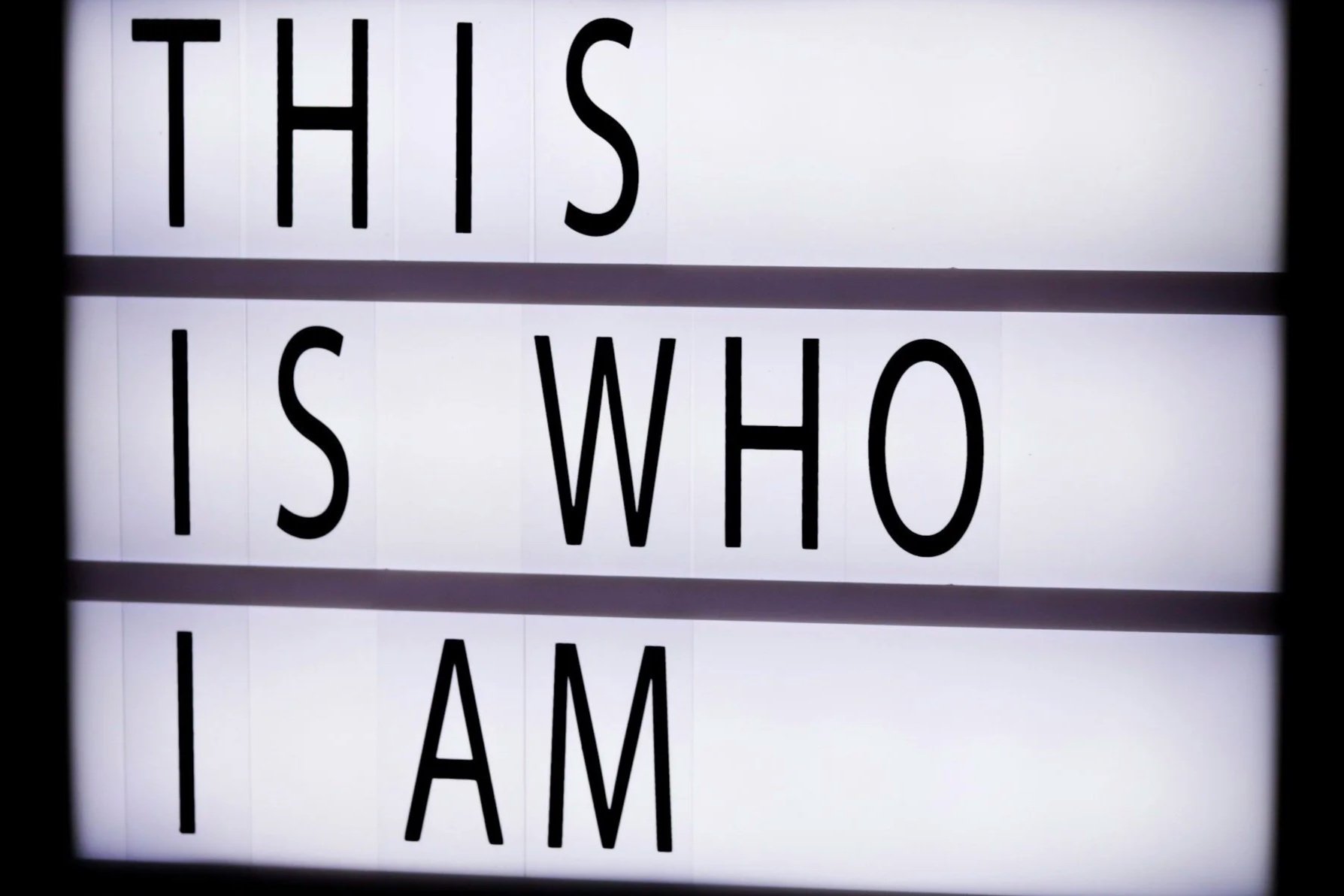 A white illuminated sign with black text that reads "THIS IS WHO I AM".