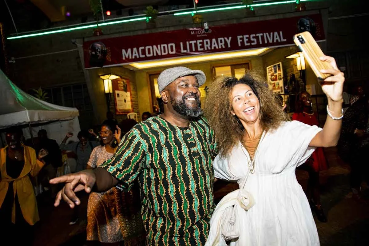 Two people taking a selfie at the Macondo Literary Festival, smiling and surrounded by festival attendees at night.