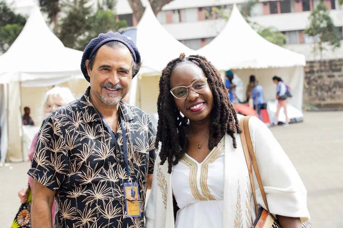 A man and woman smiling outdoors in front of white tents at an event