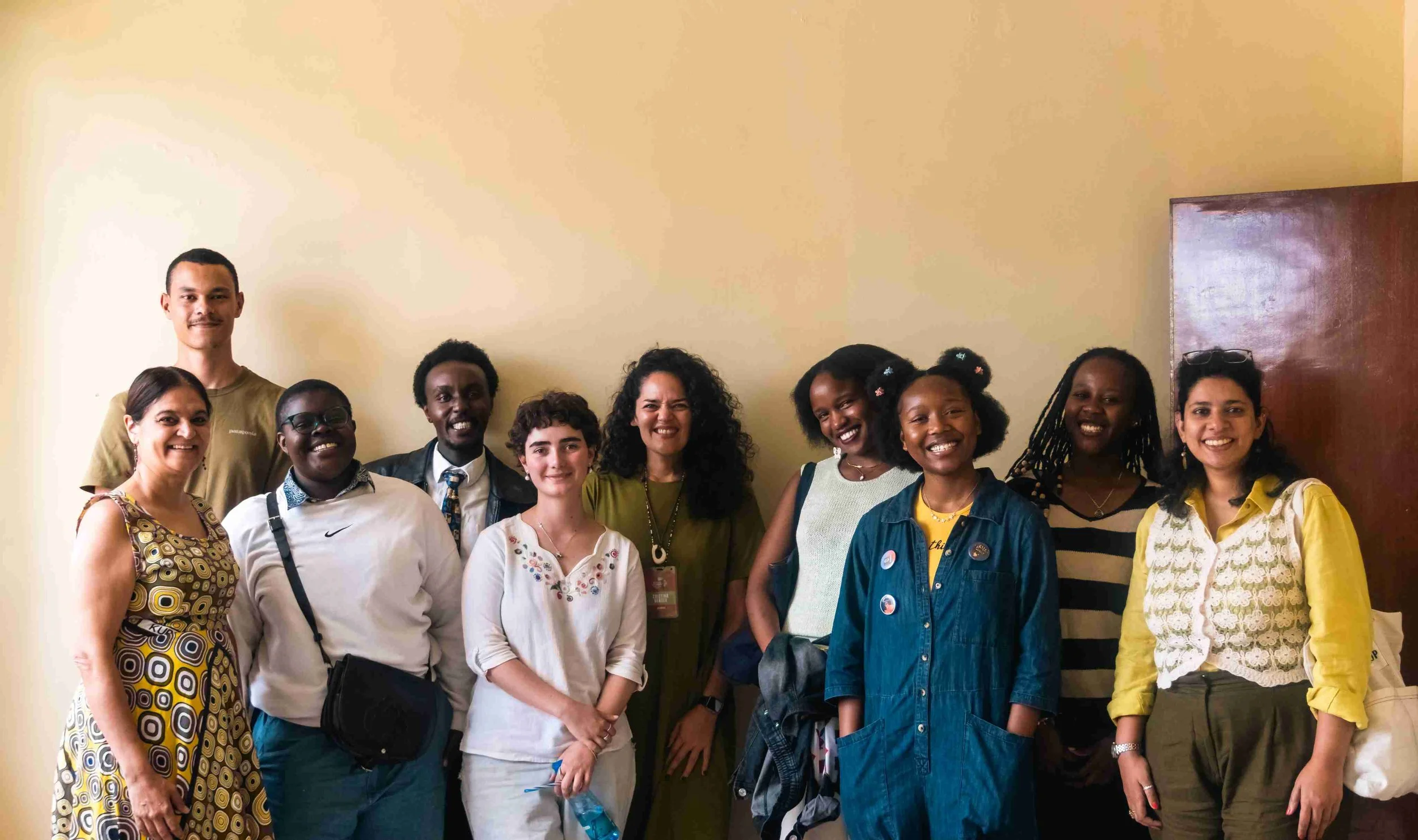 A group of ten diverse people standing together indoors, smiling for the camera.