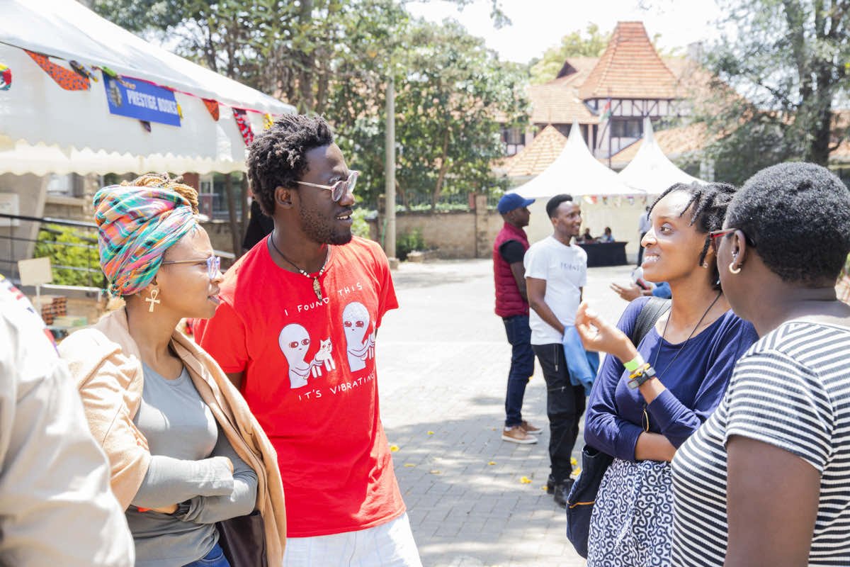 Group of people chatting outdoors at an event with white tents and a banner in the background.