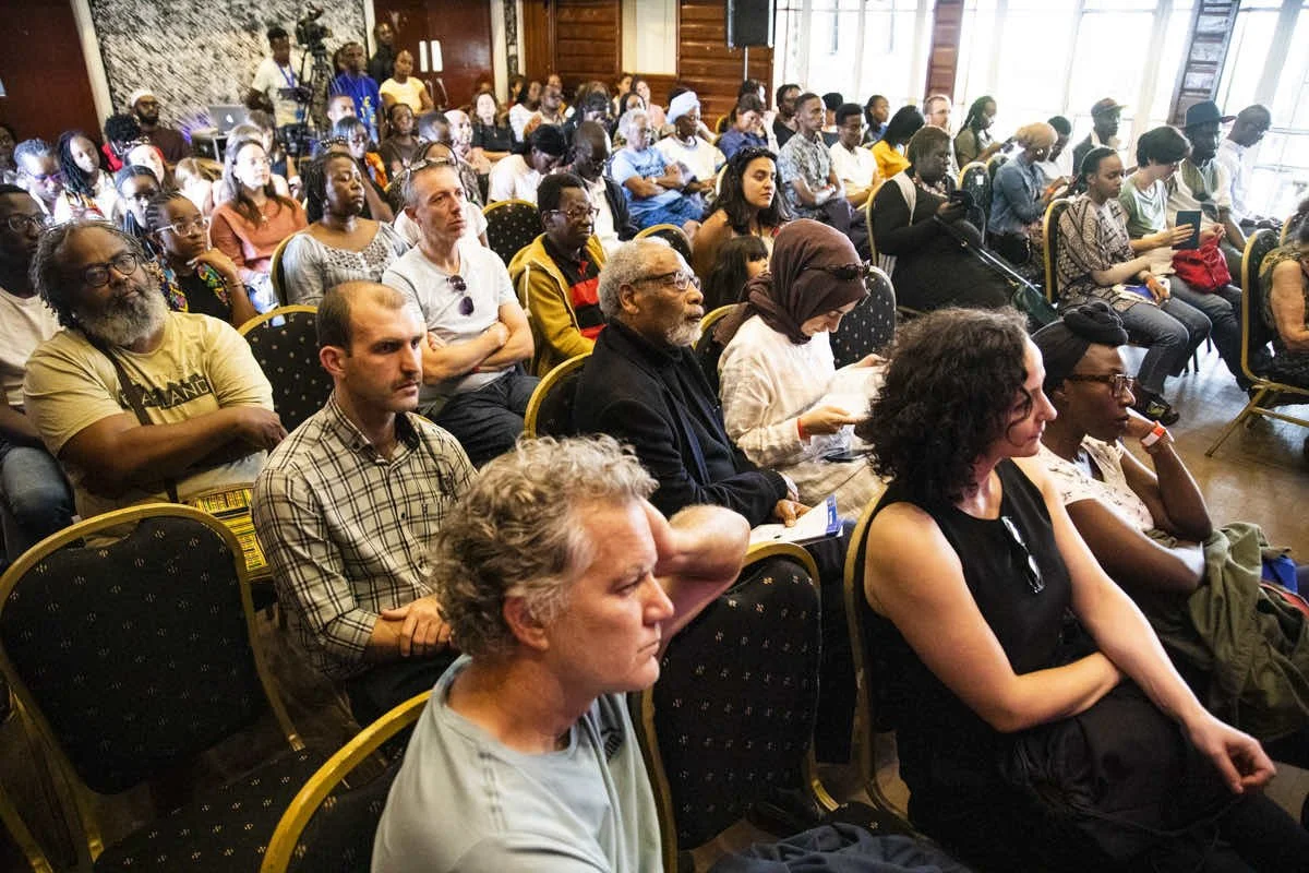 People seated in a conference room attending a lecture or presentation, with some taking notes and others listening attentively.