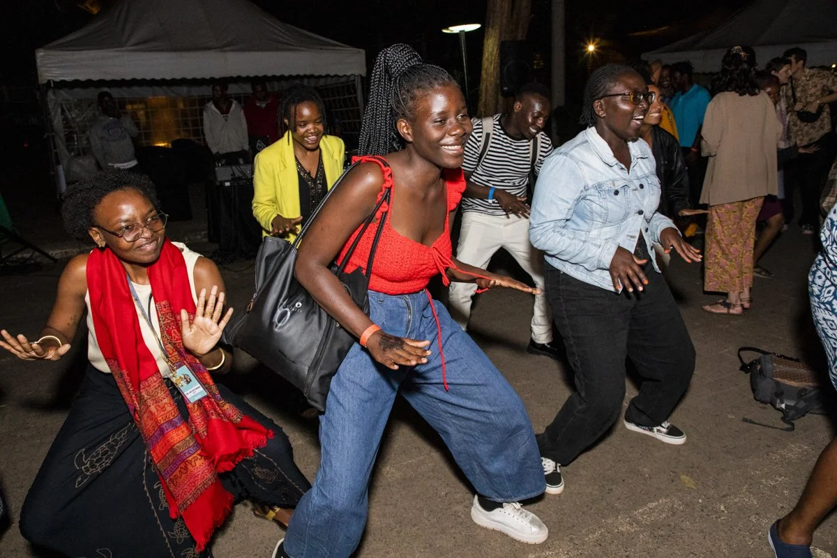 People dancing and having fun at an outdoor night event, with tents and other attendees in the background.
