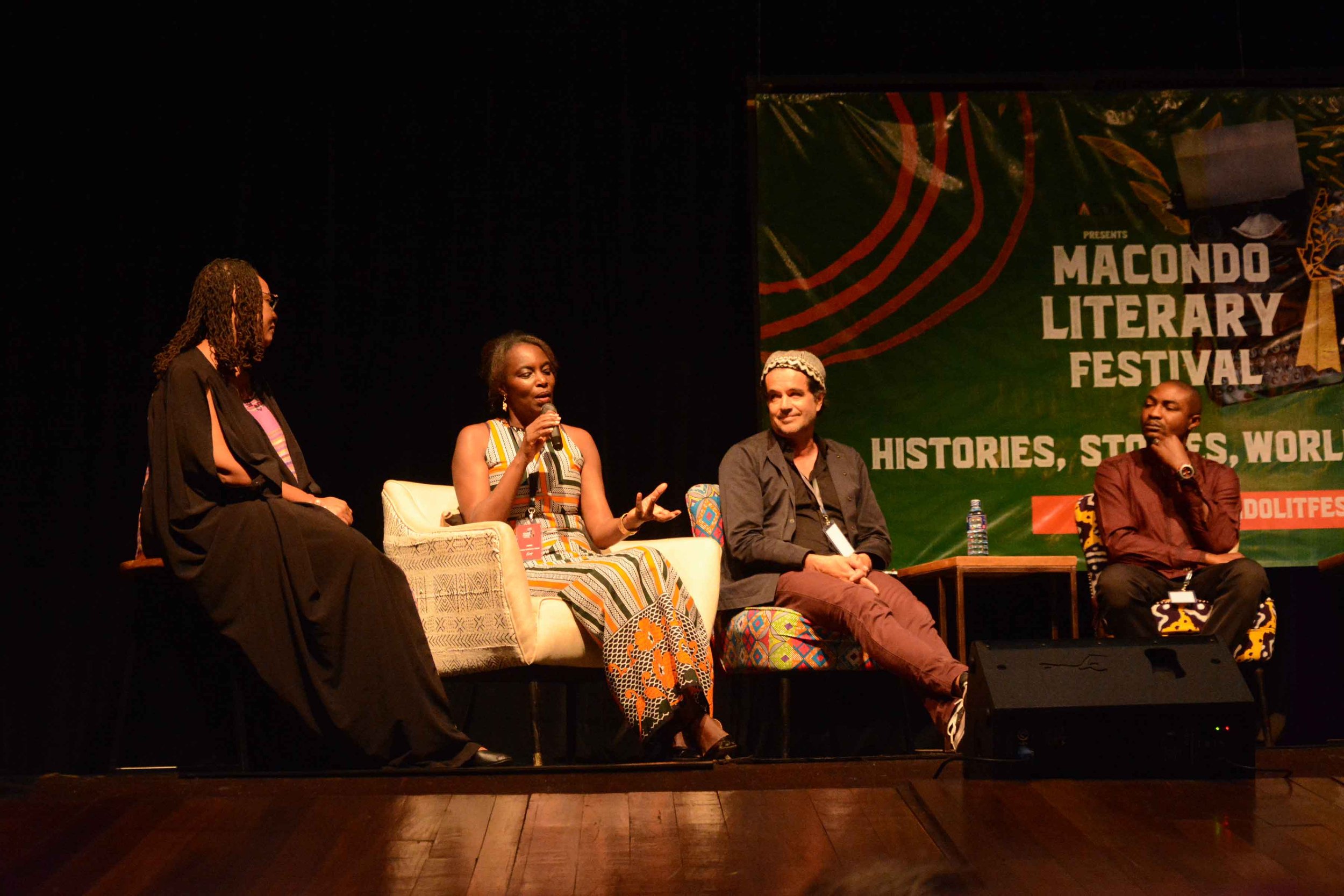 Four people sitting on stage at a literary festival panel discussion, with a sign that reads 'Macondo Literary Festival' in the background.