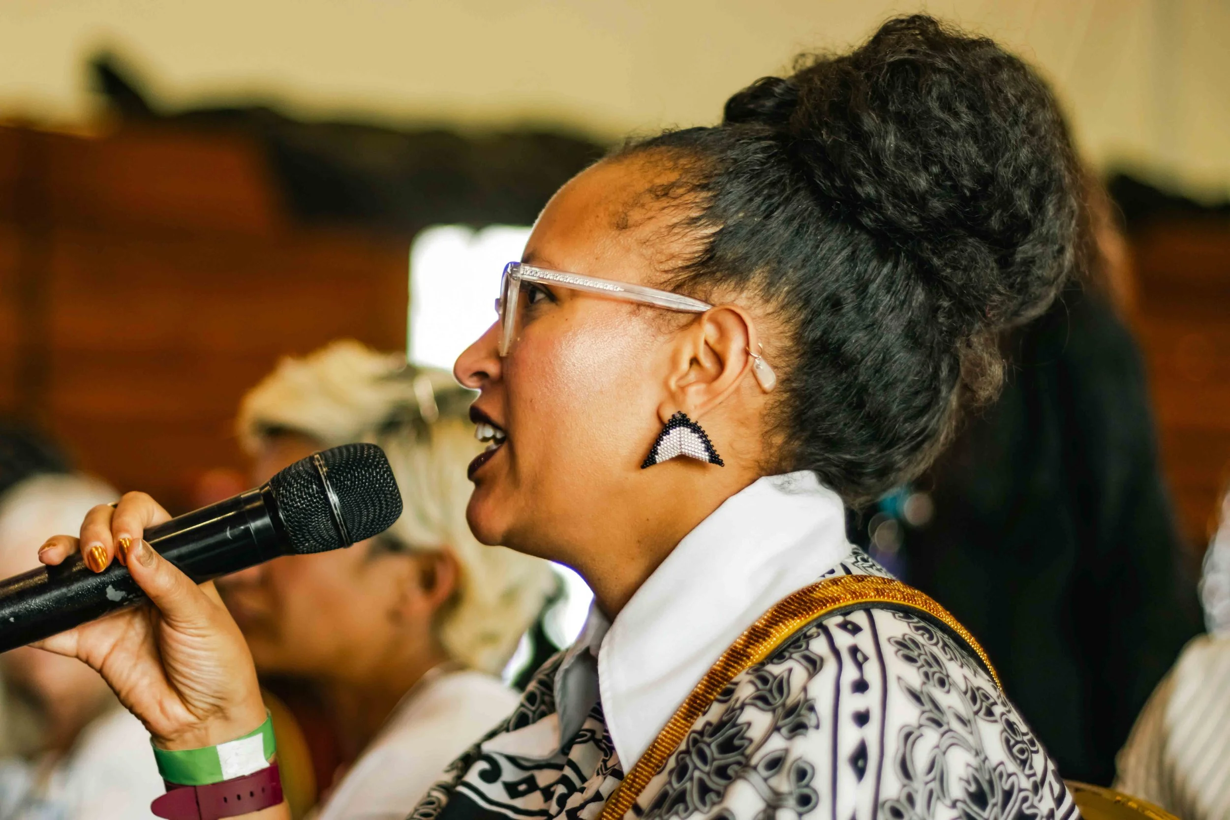 A woman with glasses and earrings speaking into a microphone at a conference or event.