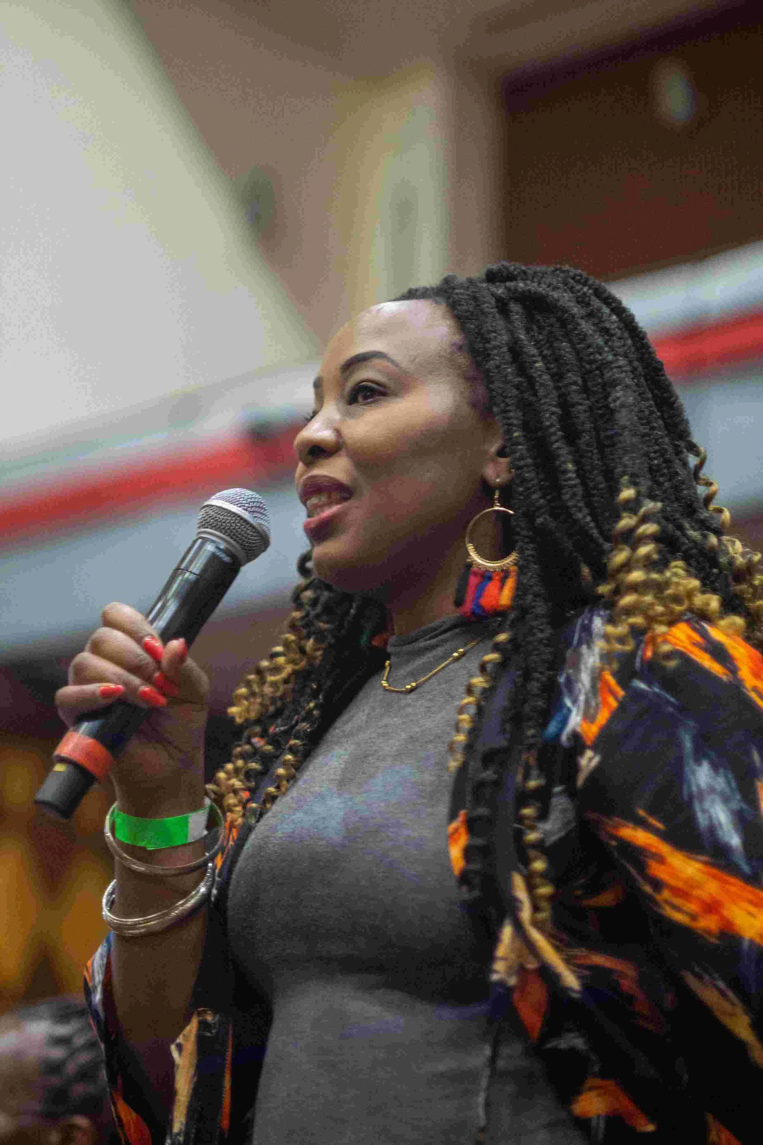 A woman with long, twisted hair, holding a microphone and speaking at an event.