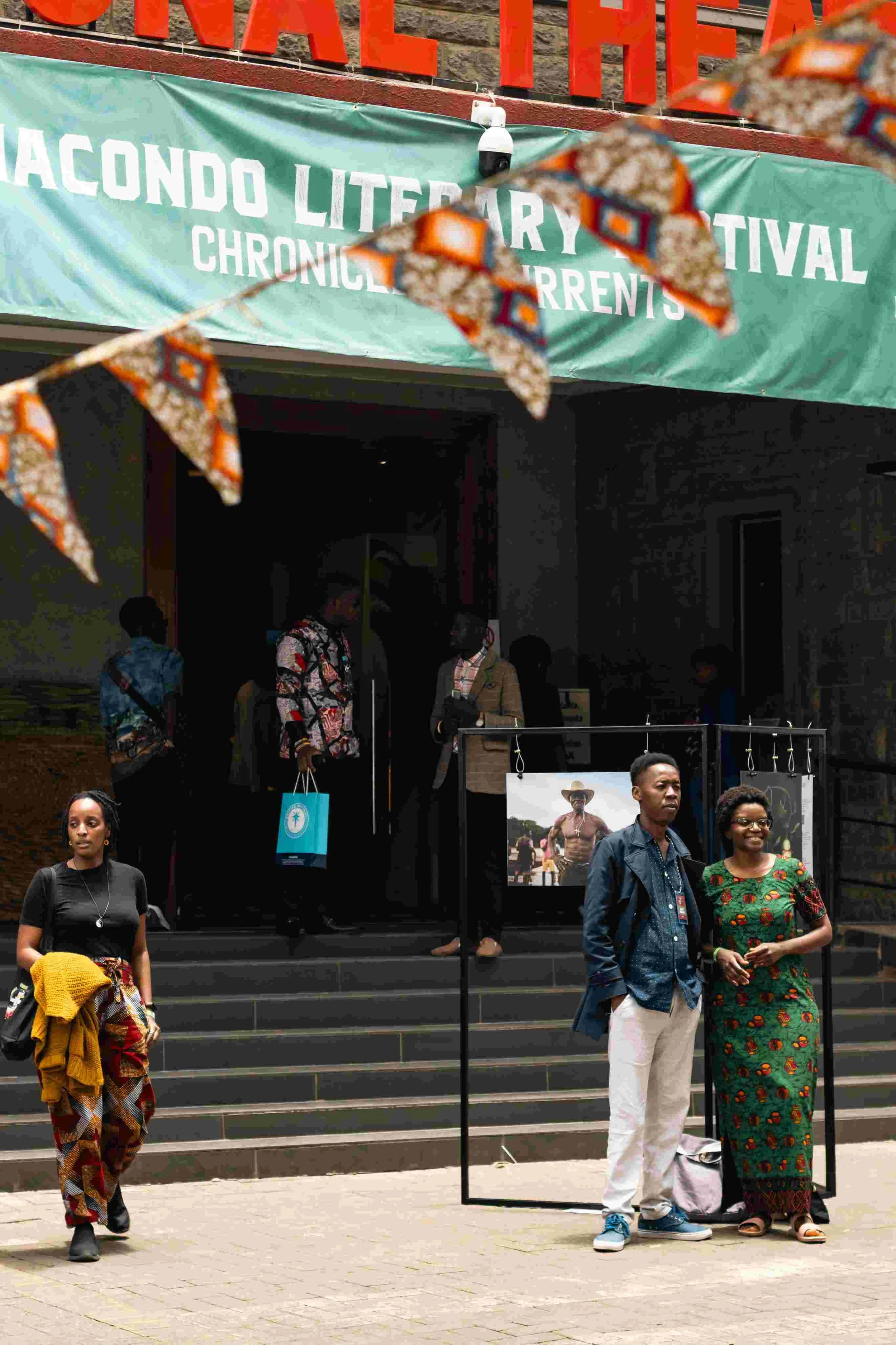 People standing outside a building with a banner that says 'Macondo Literary Festival' and a sign with an image of a man in a cowboy hat.