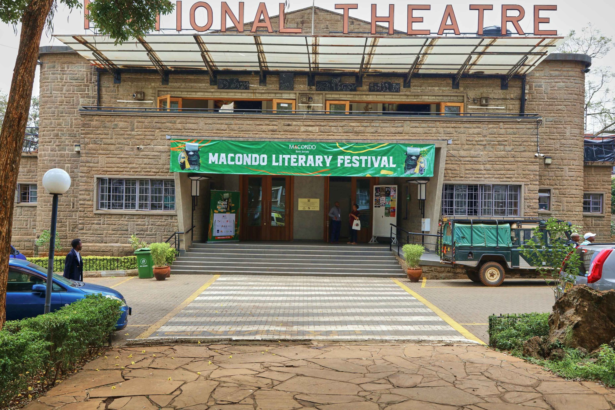 The entrance of a building with a sign reading 'National Theatre' and a green banner that says 'Macondo Literary Festival.'
