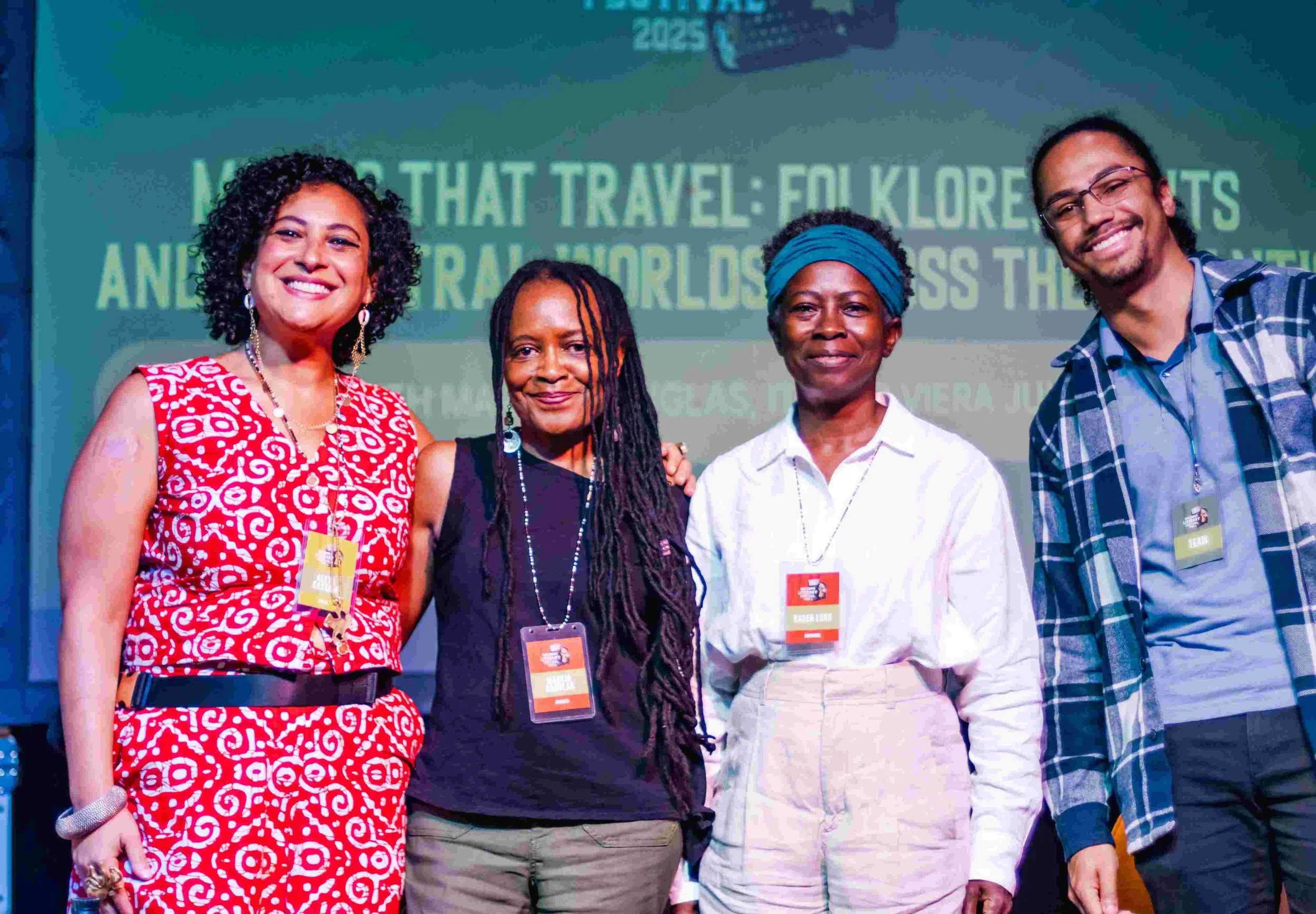Group of four women standing together at a conference or event, wearing conference badges. They are smiling, with a backdrop displaying text related to a travel event.
