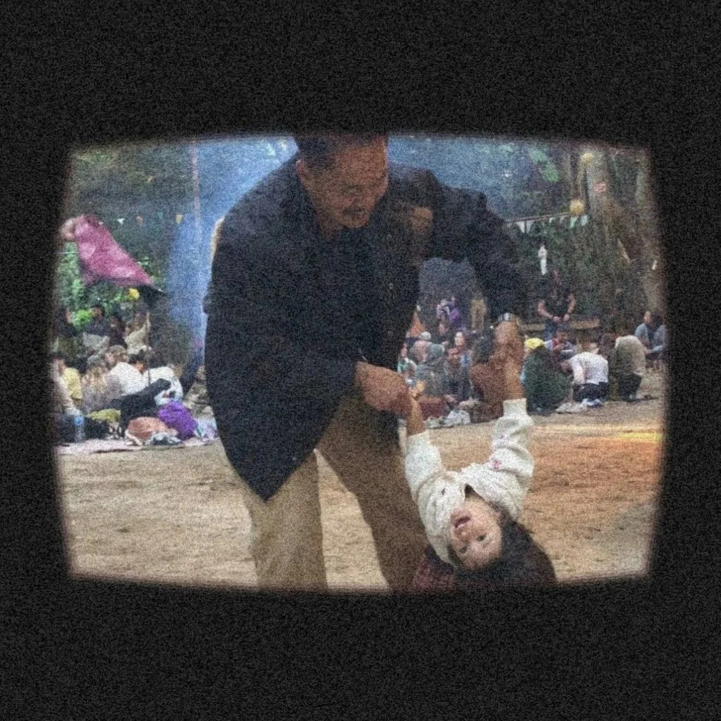 A man helping a young girl, who is upside down on the ground, at a crowded outdoor event.