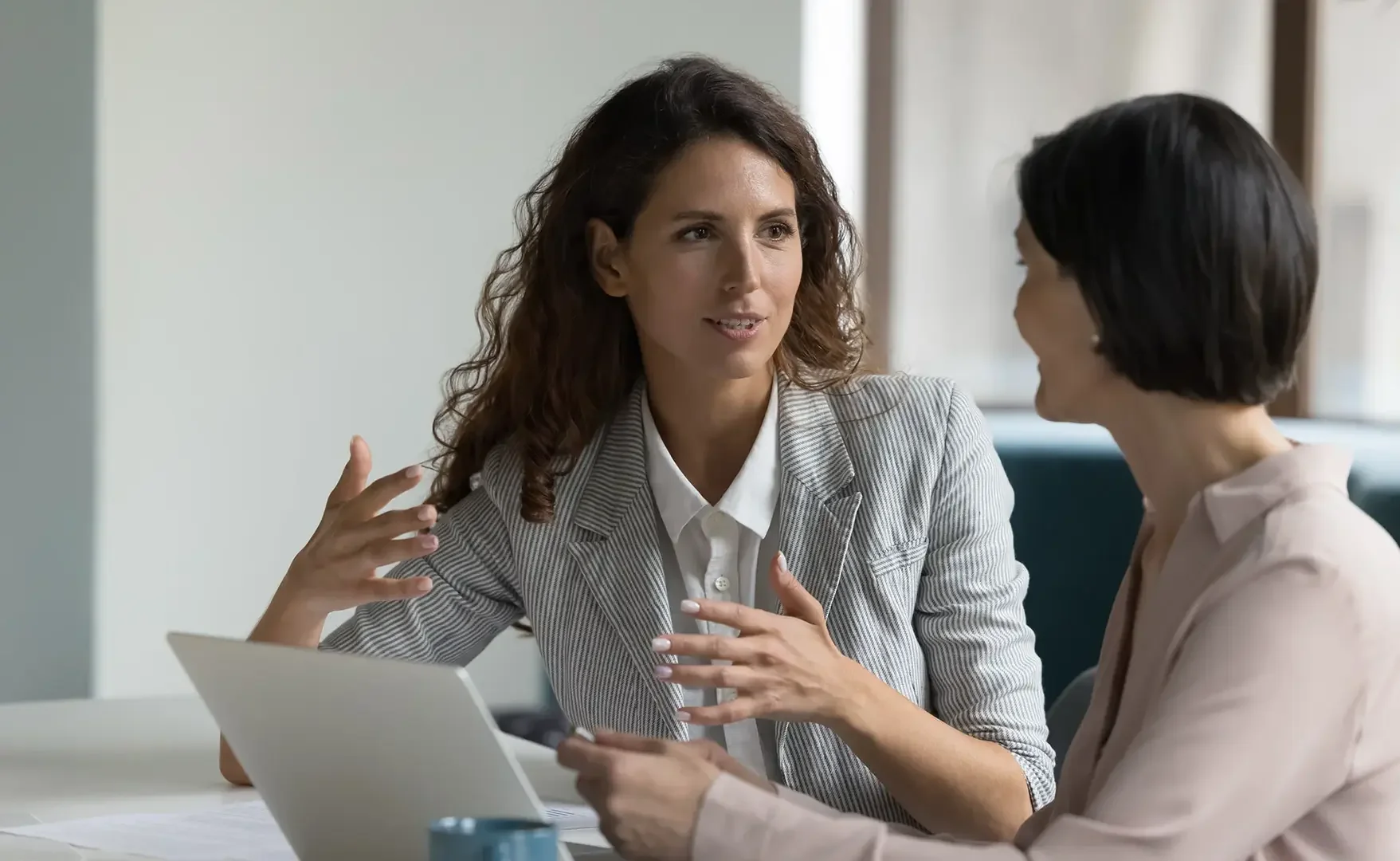 Zwei Frauen im Gespräch in einem Büro, eine hält ein Tablet, die andere gestikuliert. Bei einem Meeting oder Gespräch.
