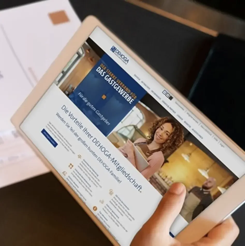 Ein Tablet, das eine Webseite der DEHOGA zeigt, mit einem Fokus auf Vorteile der DEHOGA-Mitgliedschaft im Gastgewerbe in Deutschland, mit einem Bild einer Frau im Lokal im Hintergrund.