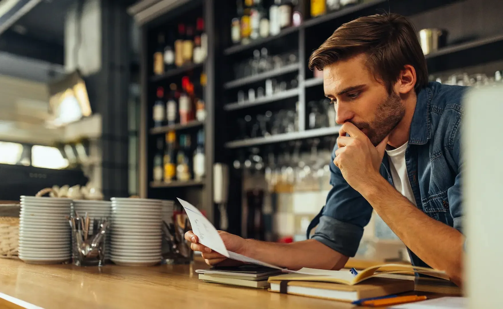 Ein junger Restaurantbesitzer liest aufmerksam ein Dokument am Tresen des Lokals.