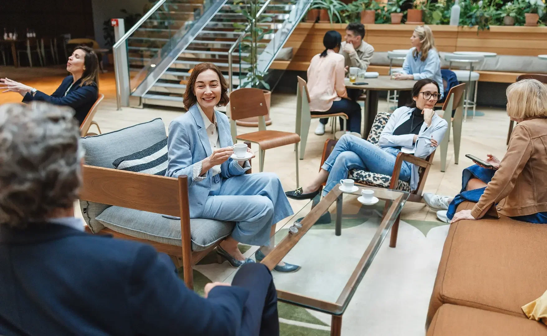 Menschen sitzen in einem Café, einige trinken Kaffee, andere chatten oder schauen auf ihre Telefone, und es gibt eine Treppe im Hintergrund.