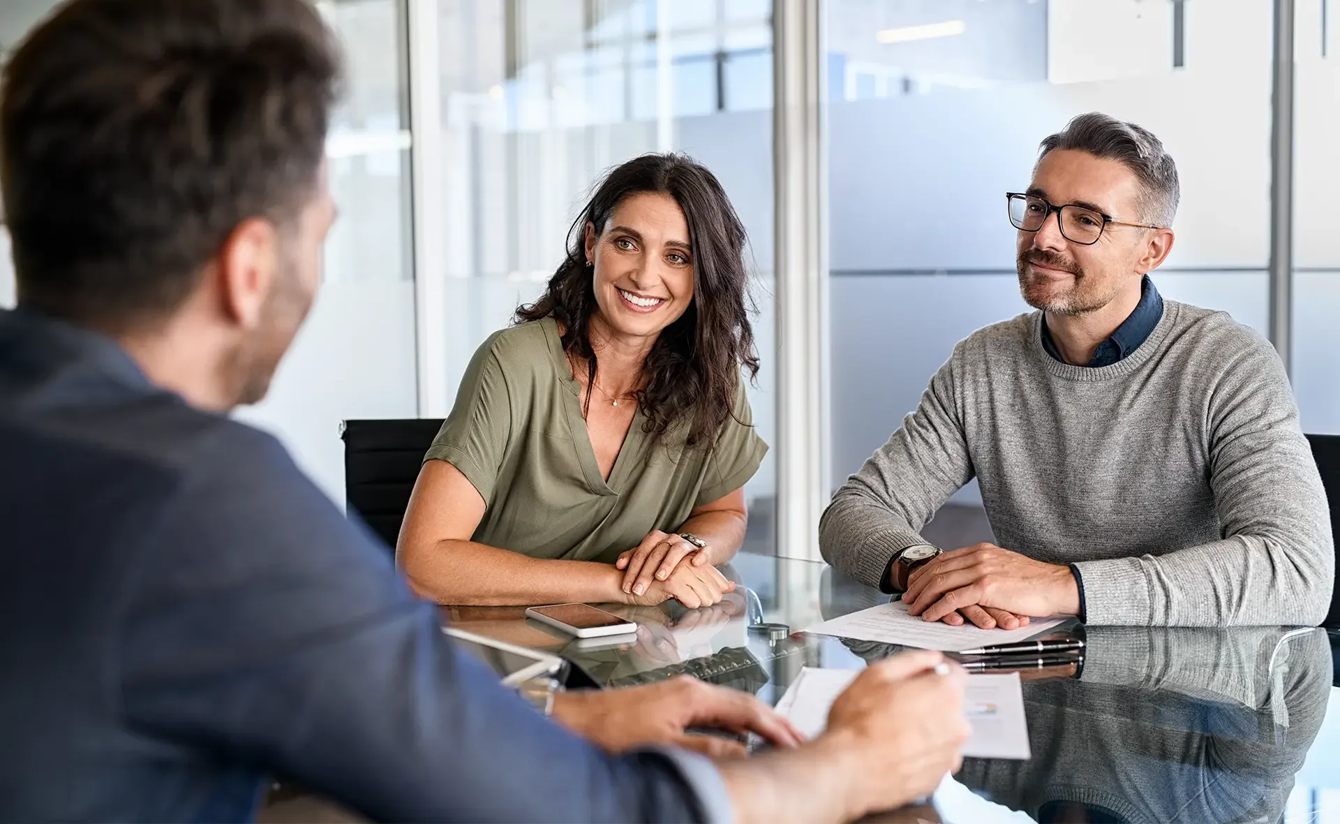 Drei Personen sitzen an einem Konferenztisch in einem Büro und führen ein Gespräch.