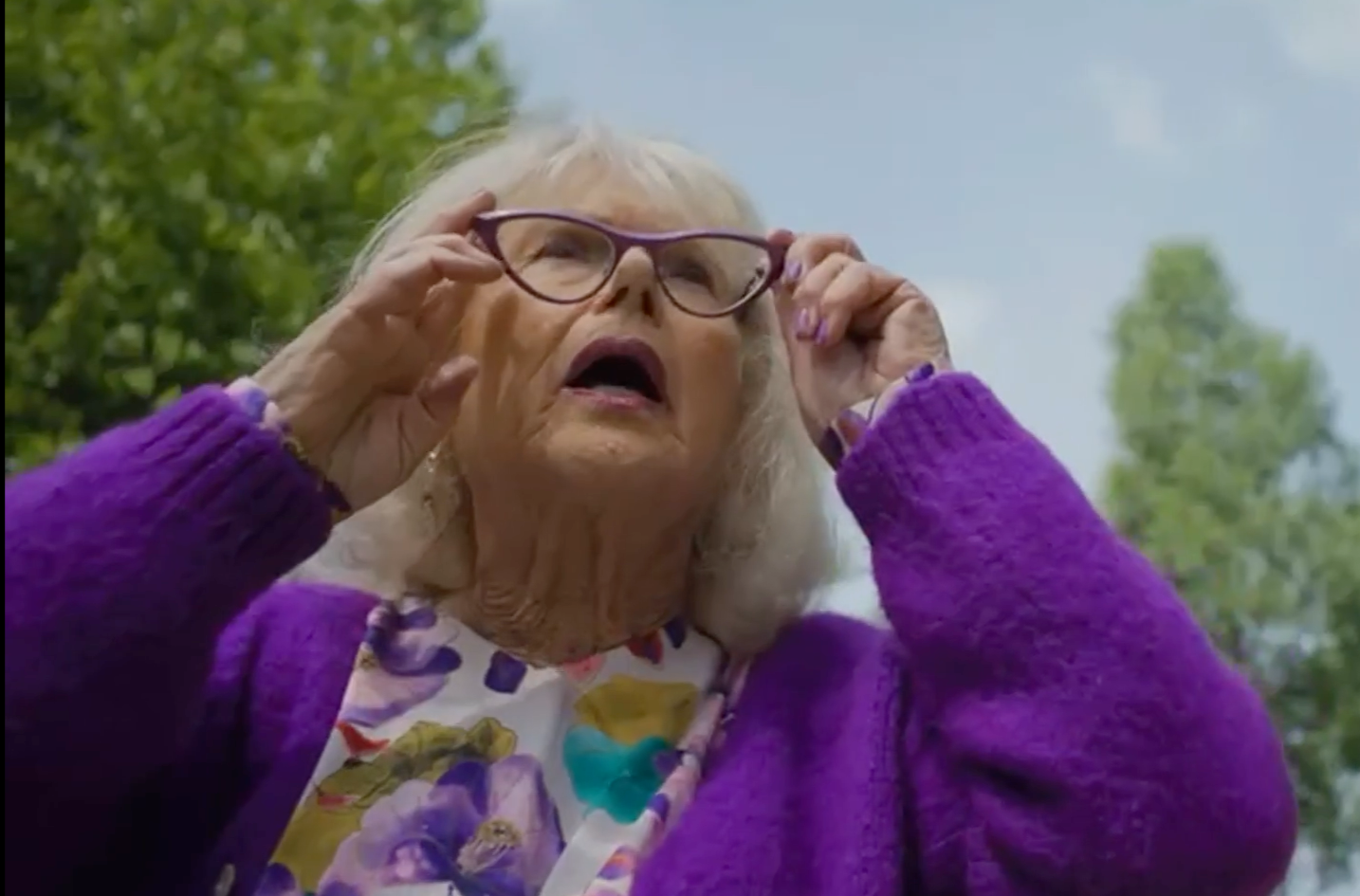 Femme âgée aux cheveux blancs ajustant ses lunettes violettes en plein air