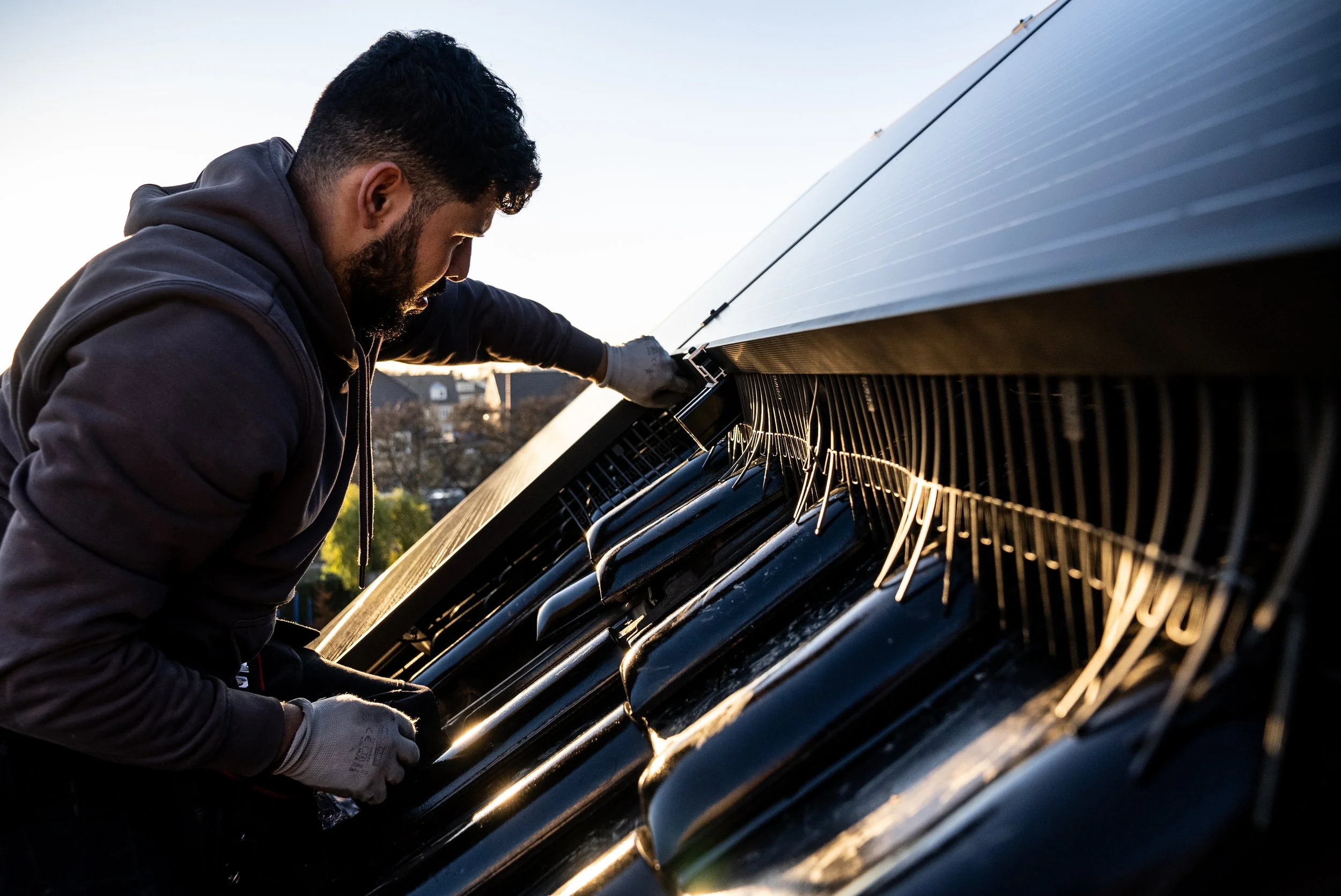 Man die een zonnepaneel installeert of onderhoudt tijdens zonsondergang. Vogelwering installatie zonnepaneel.