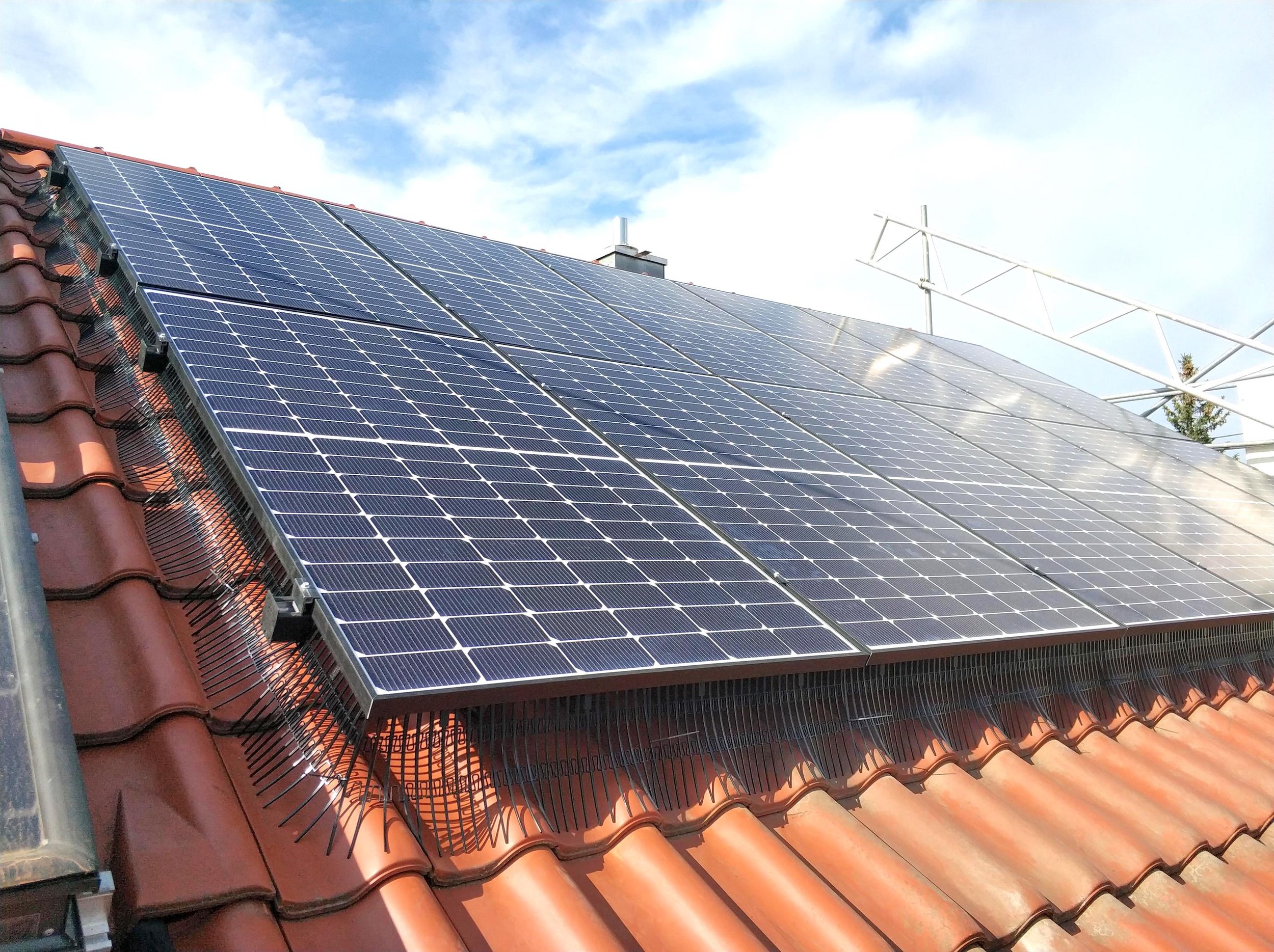 Zonnepanelen op een rood dak onder een blauwe lucht met wat wolken. Vogelwering installatie voor zonnepanelen te beschermen.