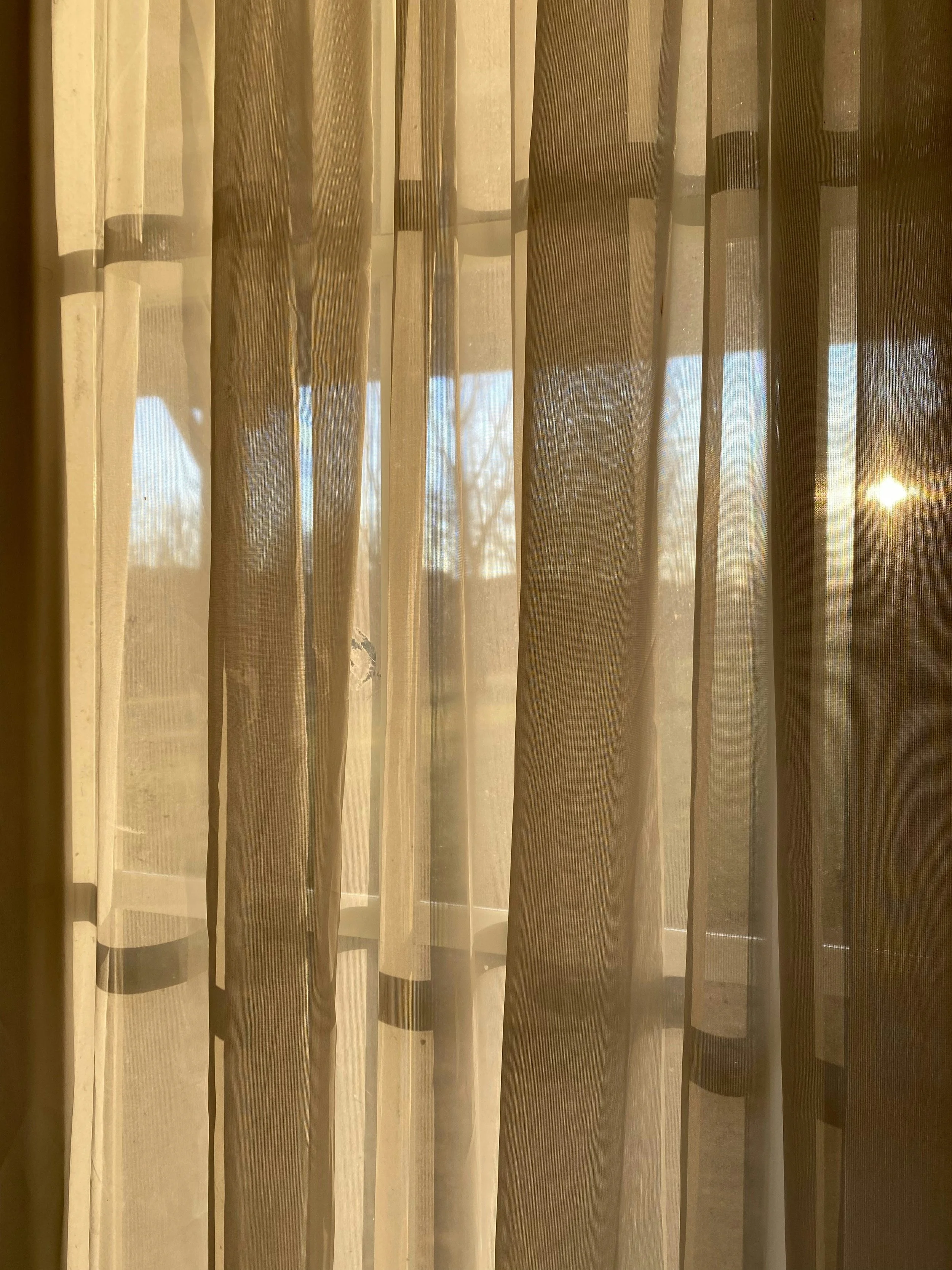 Sunlight coming through sheer curtains, creating shadows and patterns on the window and curtain folds.