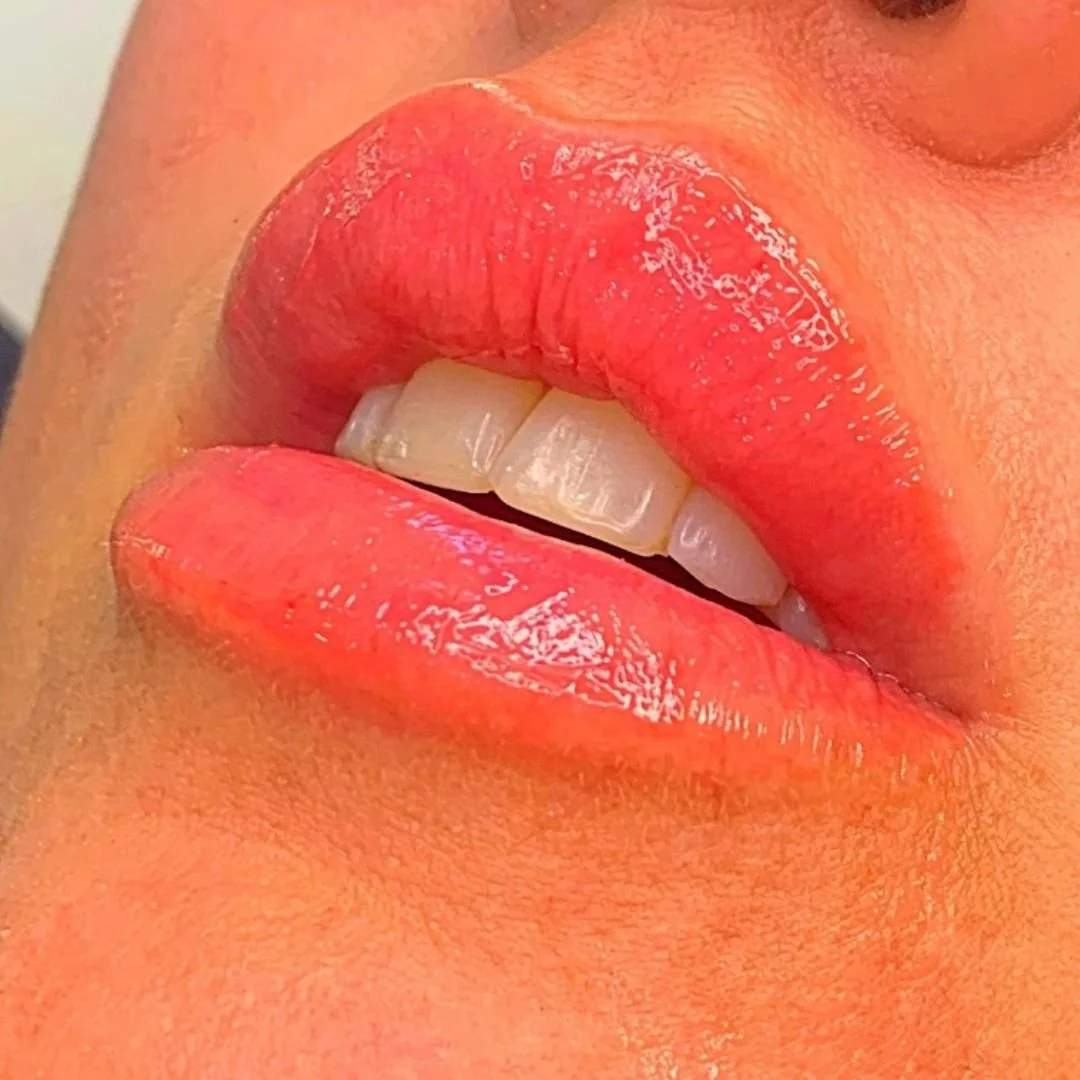 Close-up of lips with glossy pink lipstick slightly open to reveal teeth.