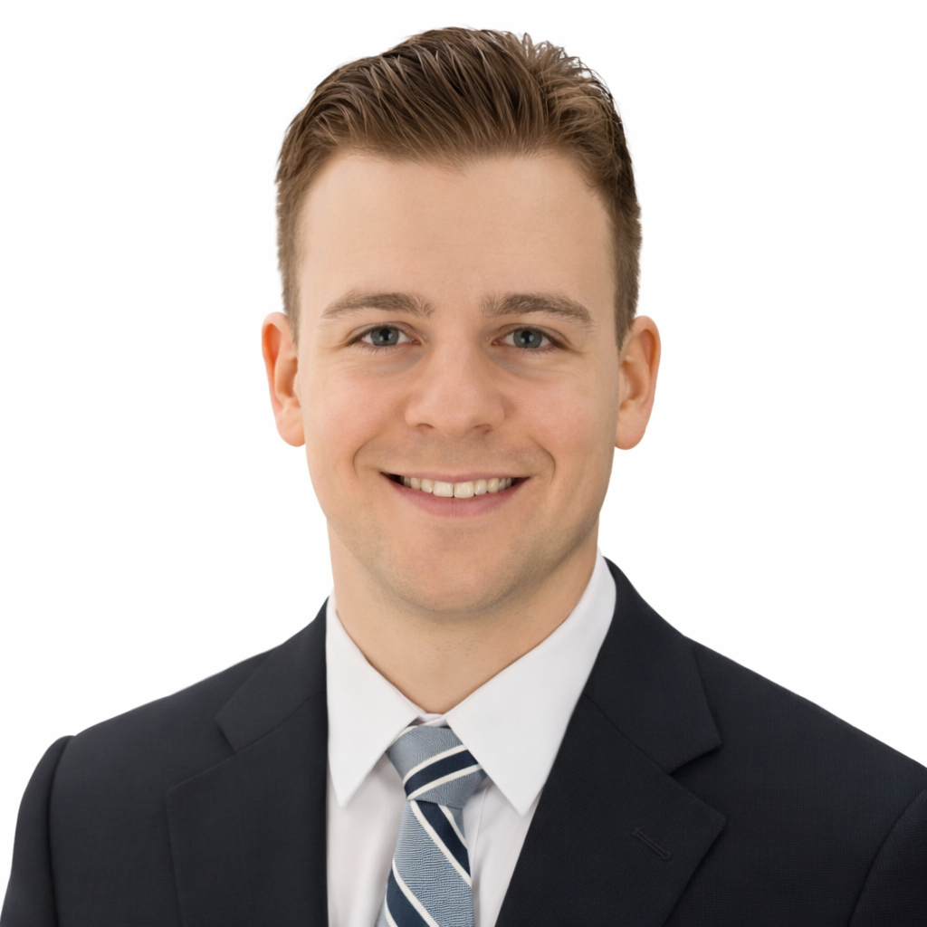 A professional portrait of a young man with short, brown hair, wearing a black suit, white shirt, and a striped ties, smiling at the camera against a plain white background.