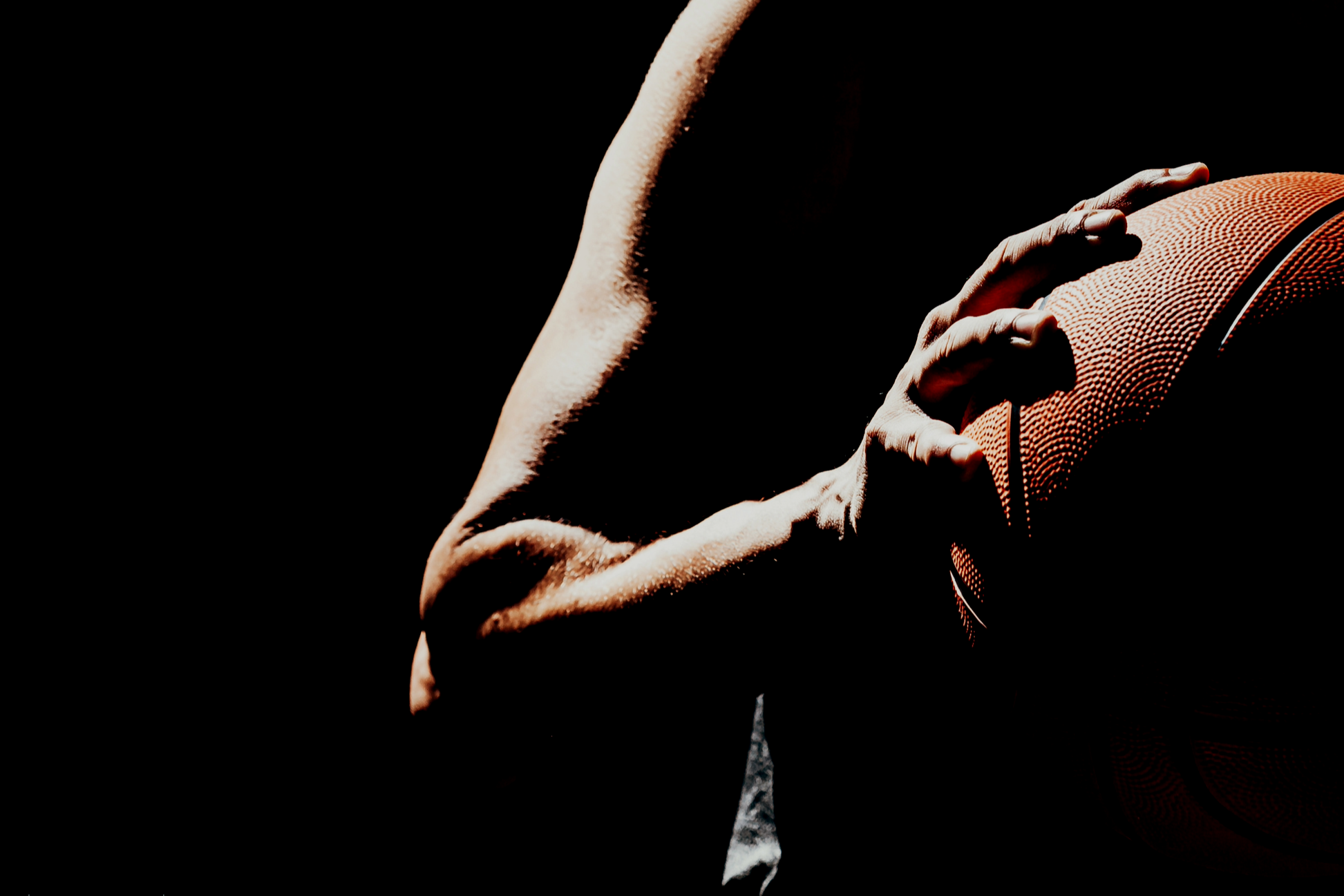 A person holding an American football with one arm, shot in low light with a dark background.