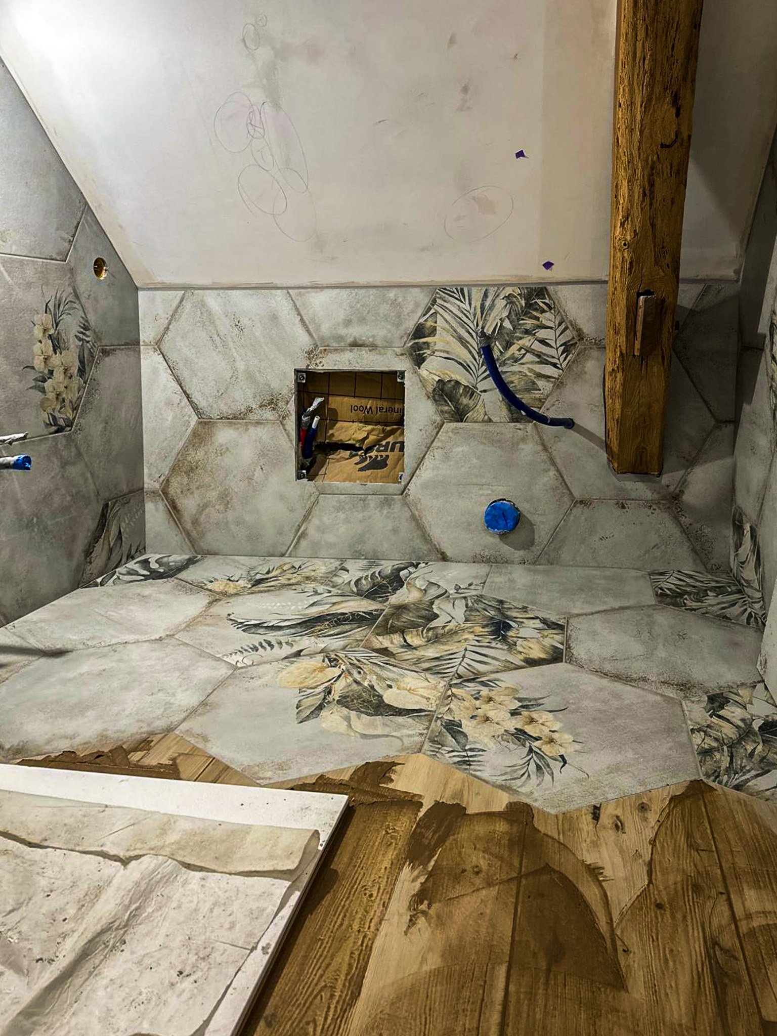 Intérieur en rénovation d'une salle de bain avec des carreaux de ciment à motifs floraux, un trou dans le mur, des tuyaux apparents et une structure en bois.