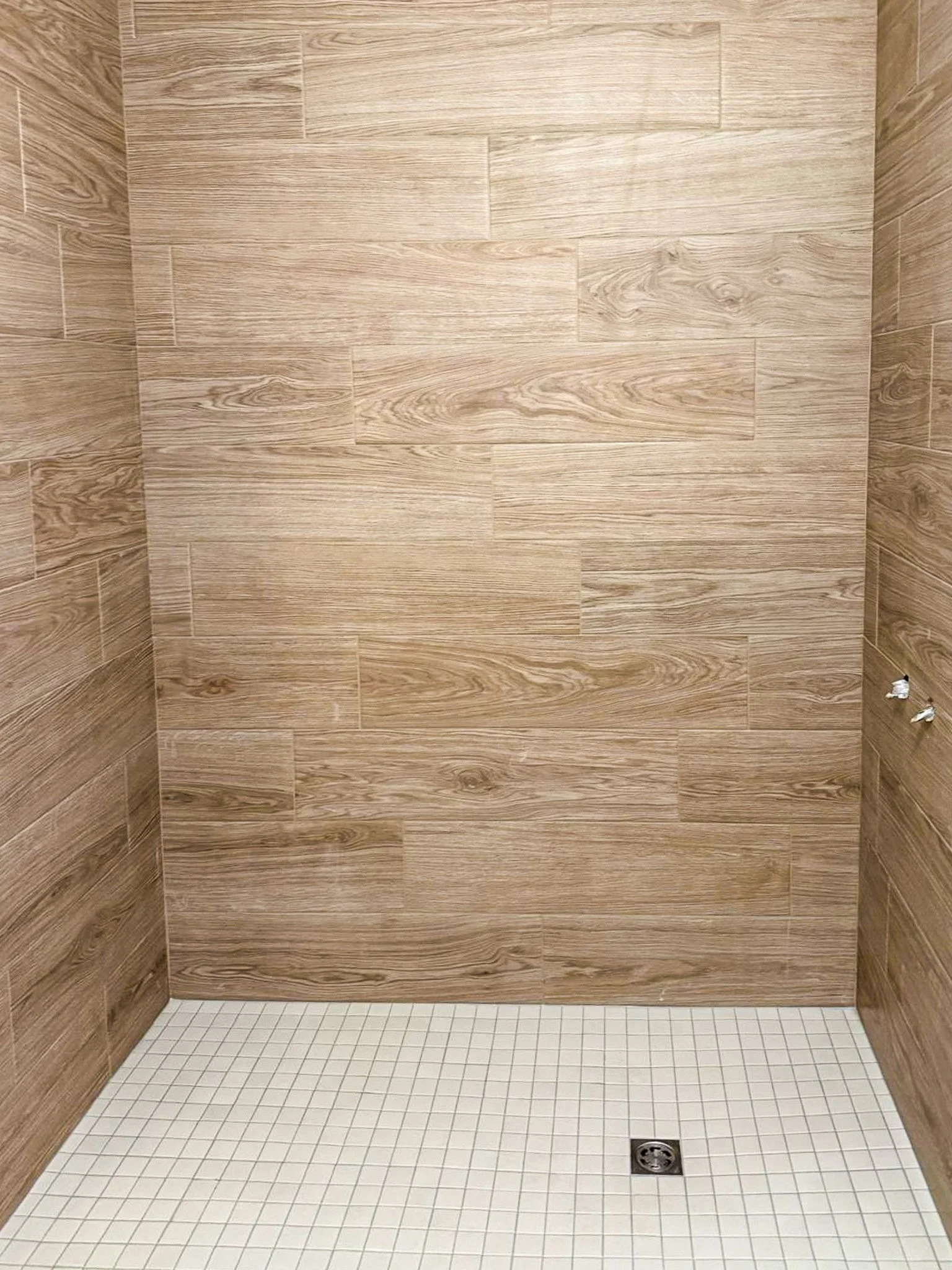 Une douche avec des murs en carrelage imitation bois et un sol en petits carreaux blancs, avec un drain au centre