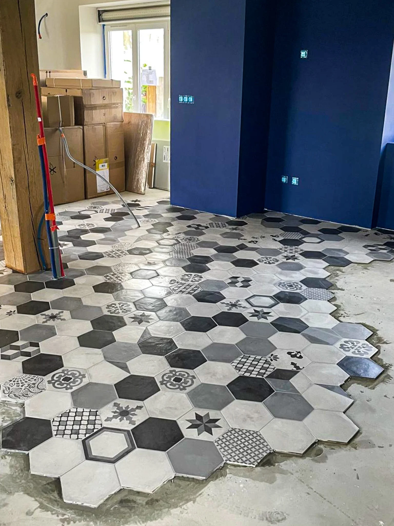 Pose de carreaux hexagonaux noirs, blancs et motifs sur le sol d'une pièce en rénovation.