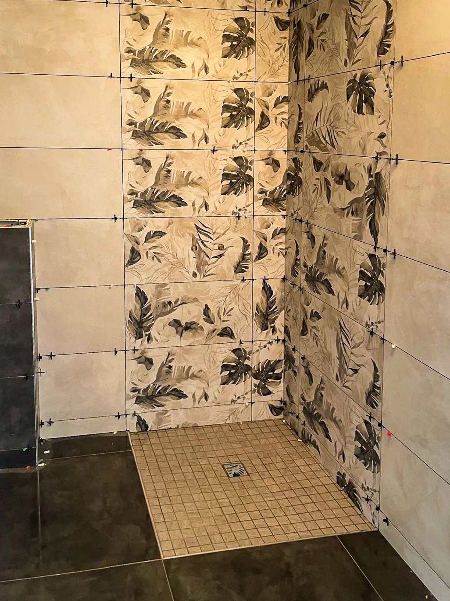 Pose d'une nouvelle mosaïque de carreaux de sol dans une salle de bain, en préparation pour la pose de carreaux muraux avec un motif de feuilles tropicales sur la partie du mur.