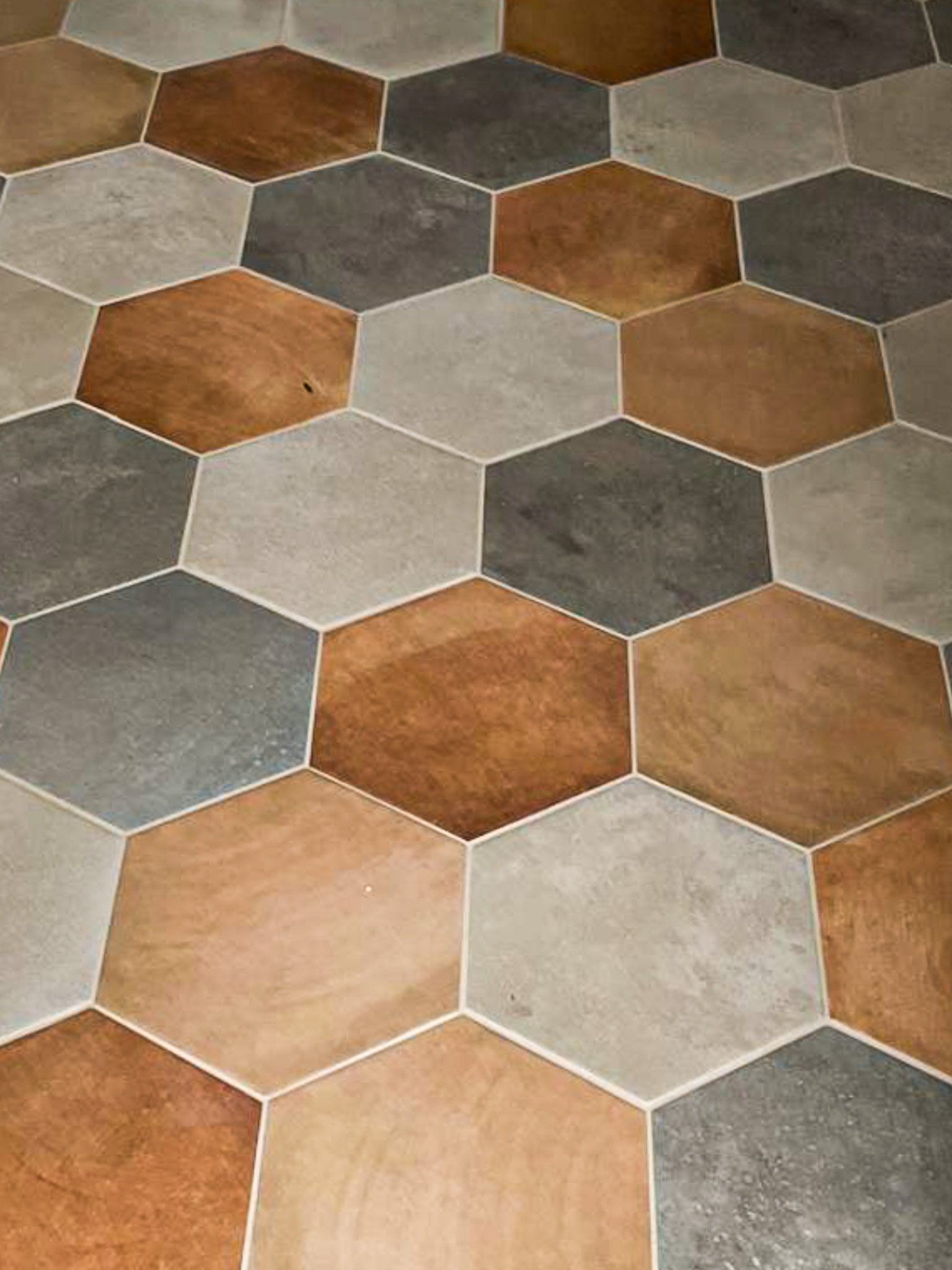 Tuiles de sol hexagonales de différentes couleurs, notamment gris, beige, marron et noir.