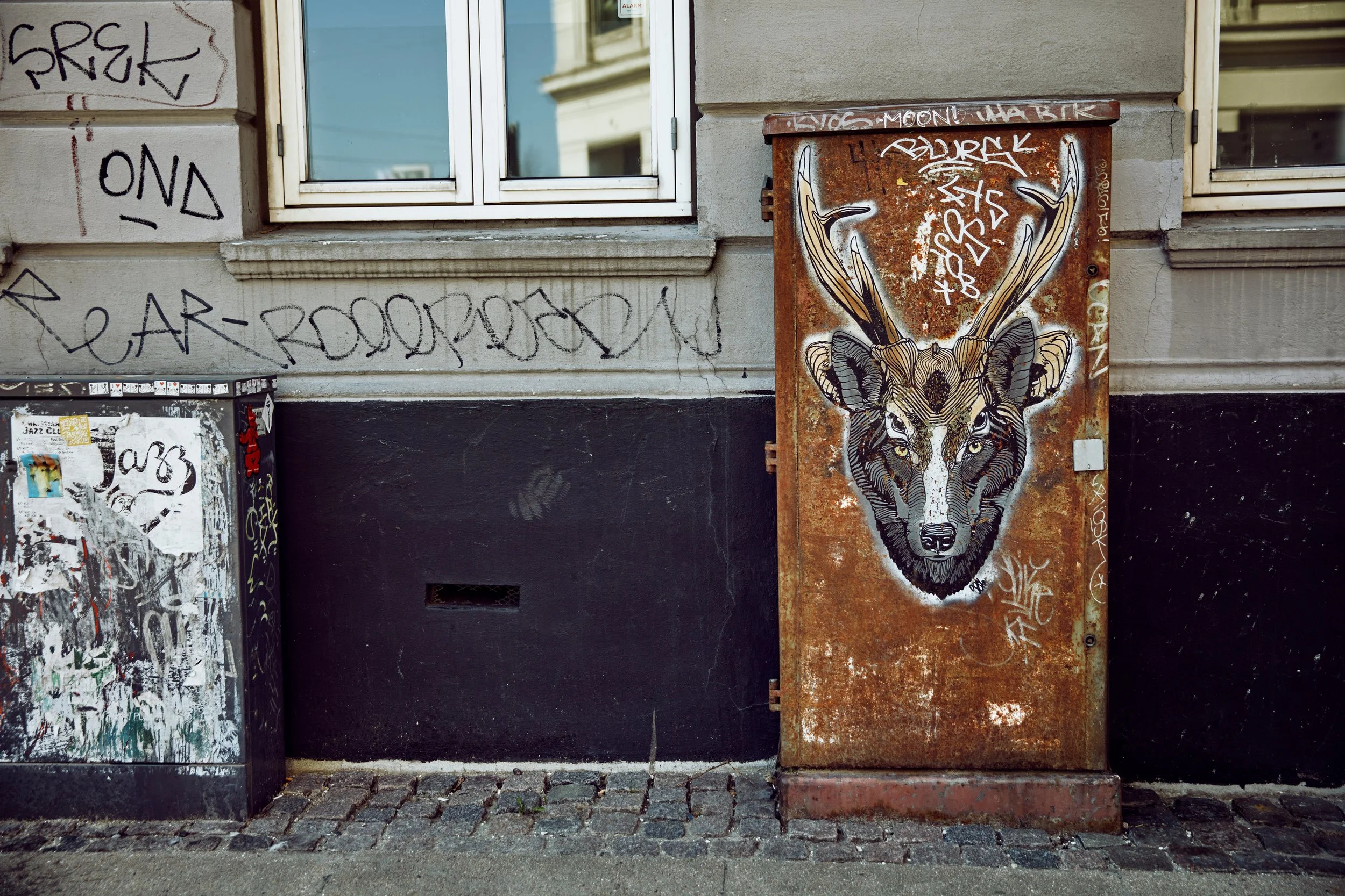 Gademurværing med graffiti og et malt billede af en hjort med stor gevir på en rusten metal-telefonboks.